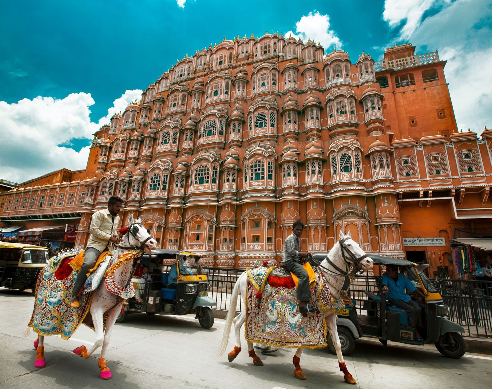 Hawa Mahal, Jaipur, with its distinctive pink facade and numerous windows, with two decorated horses in the foreground.
