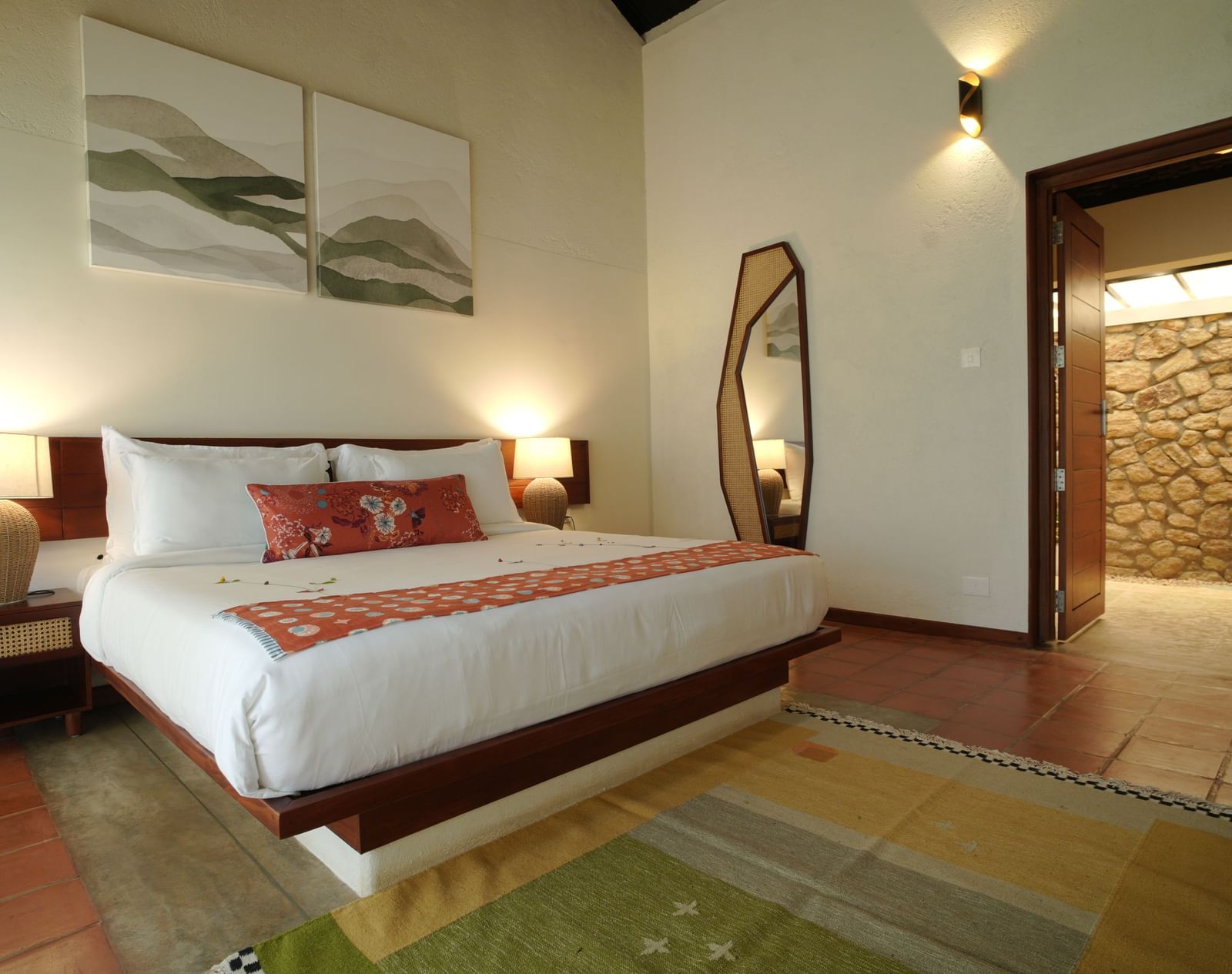  A well-appointed bedroom at Vaasta Vagamon featuring a large bed, bedside tables with lamps, a floor-length mirror, and artwork.