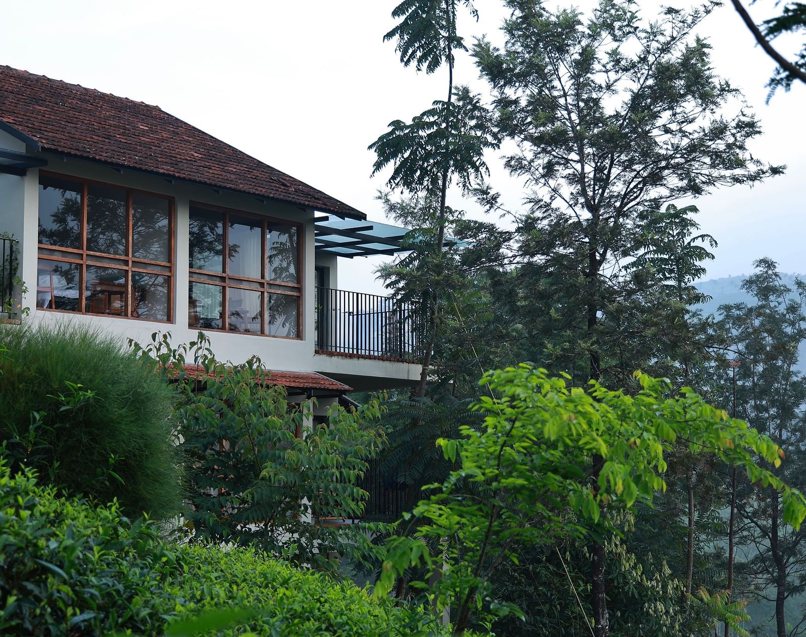  A building at Vaastha Vagamon, nestled amidst abundant foliage, with large windows overlooking a verdant landscape.