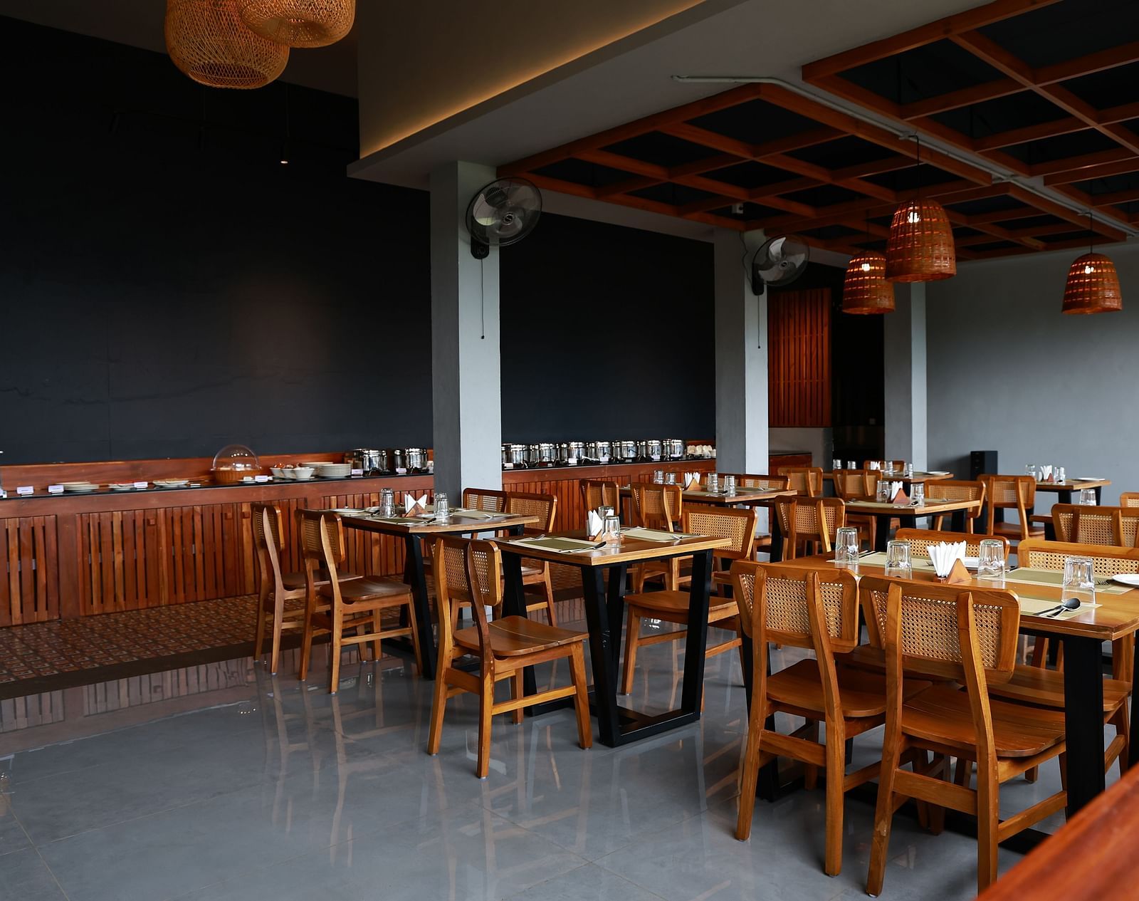 A well-appointed dining area at Vaastha Vagamon, featuring numerous tables and chairs, a buffet spread, and modern lighting fixtures.