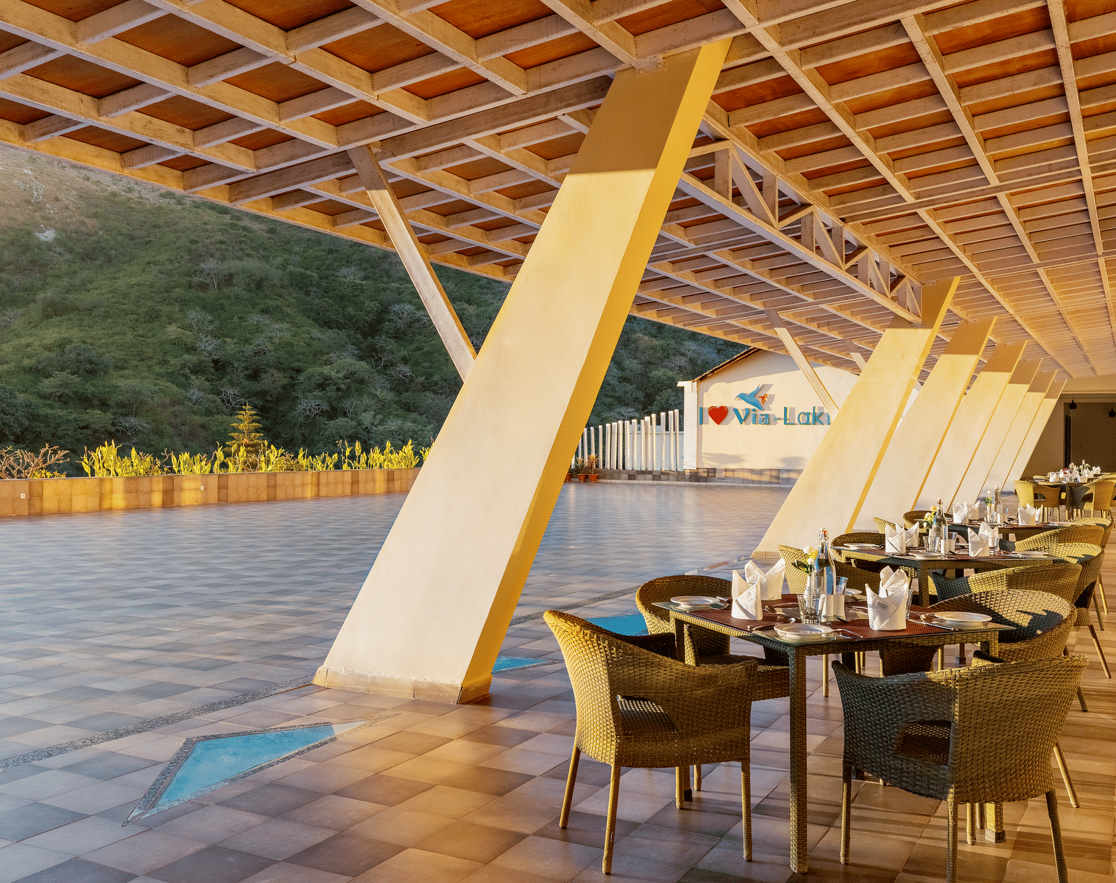 An outdoor dining area with tables and chairs under a covered patio, overlooking a landscape - Via Lakhela Resort & Spa, Kumbhalgarh