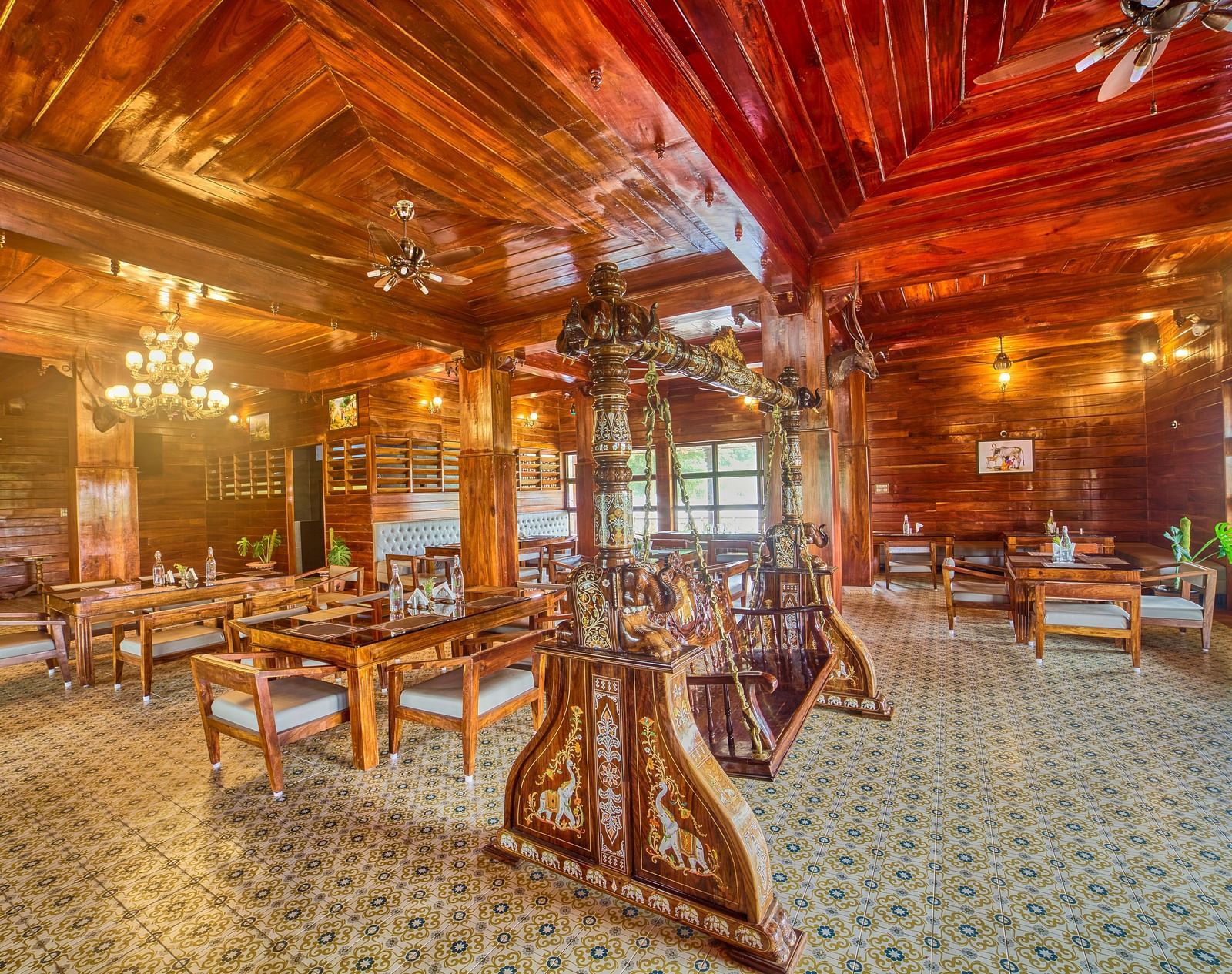A spacious, rustic-style dining or common area with polished wooden floors, exposed wooden beams and columns, and multiple tables and chairs set up for guests, viewed from a different angle. - Vintage Trails by Ilara