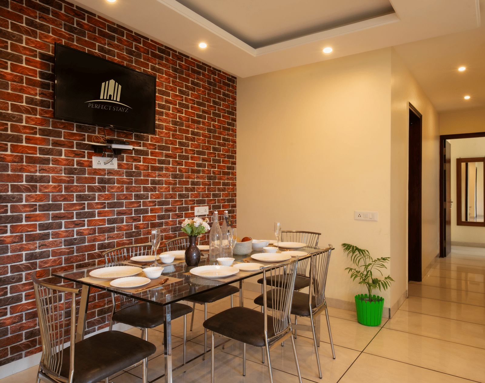 A dining area with a brick wall, a wall-mounted television, a dining table, and chairs at Perfectstayzz Value Shimla (Namah Retreat).