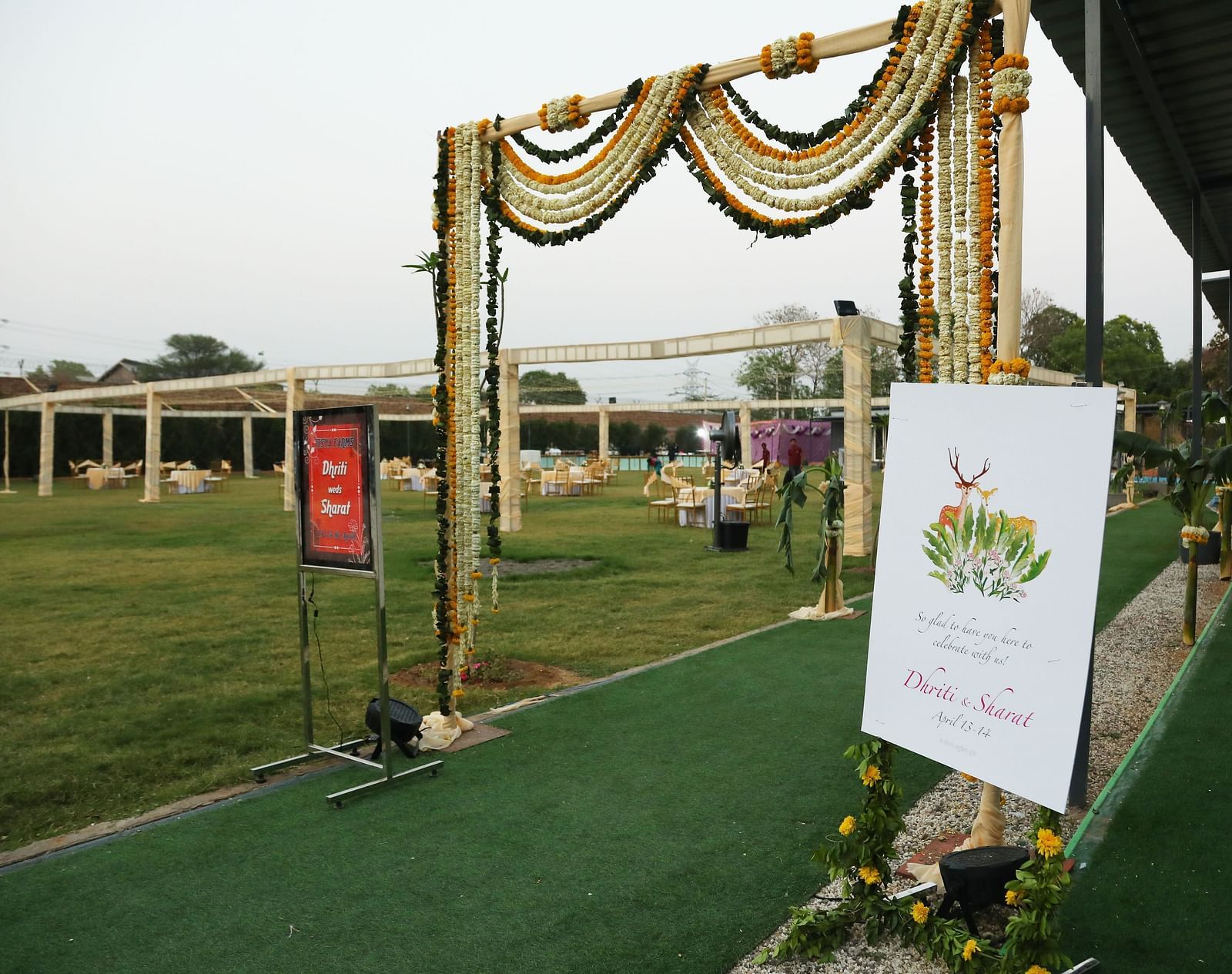 An entrance setup at Tisya Farms, Gurgaon with green flooring, flower decorations, and a welcome board.