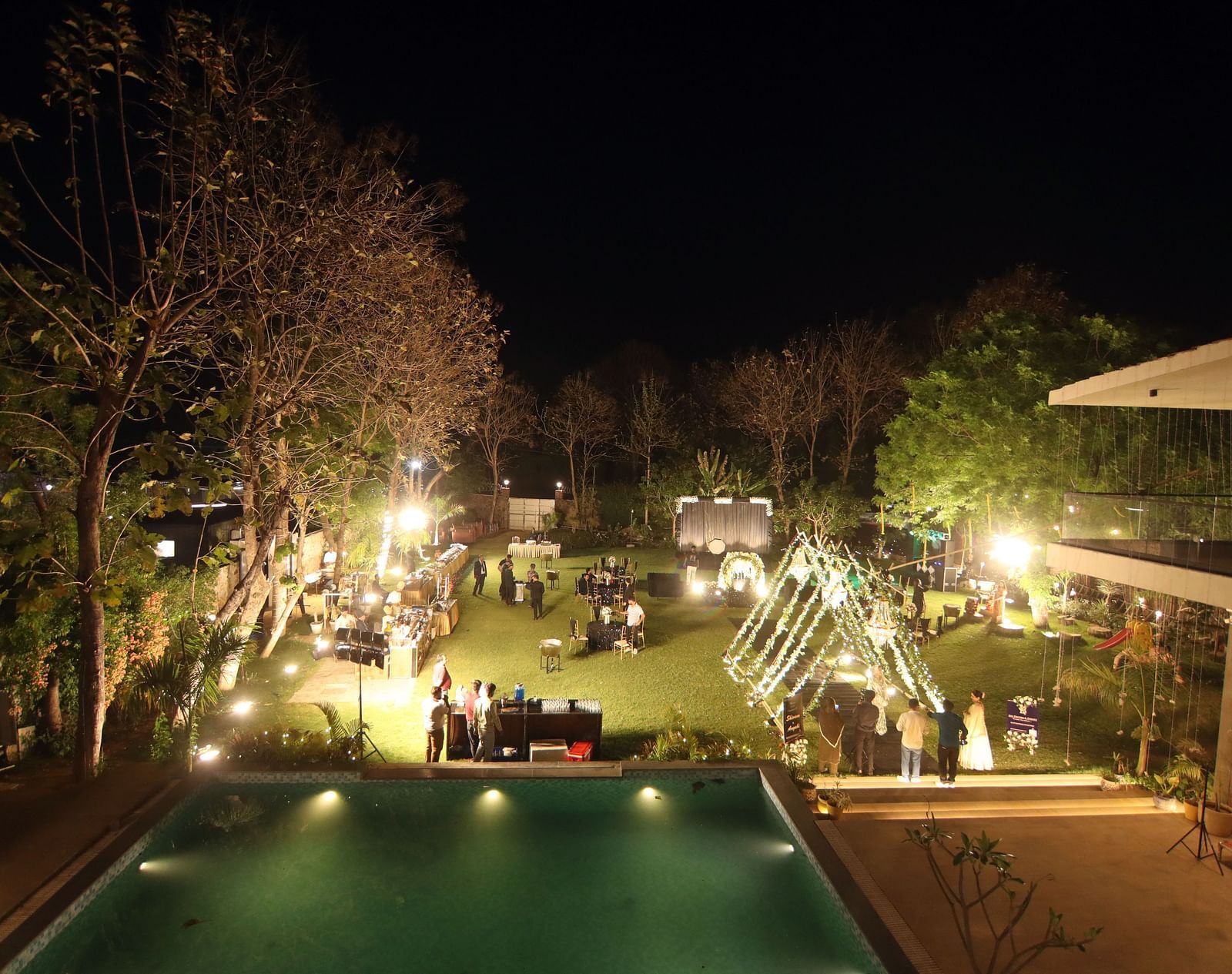 Elevated poolside view at night with event lighting and lawn setup at Tisya Farms, Gurgaon.