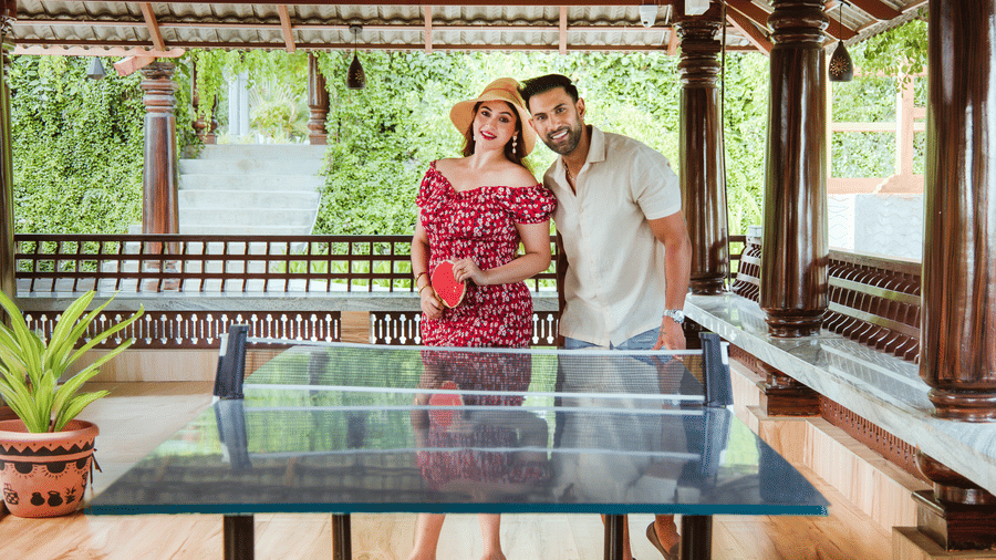 A man and a woman standing next to a table tennis table in a sheltered outdoor area with wooden pillars | Vintage Trails By Ilara