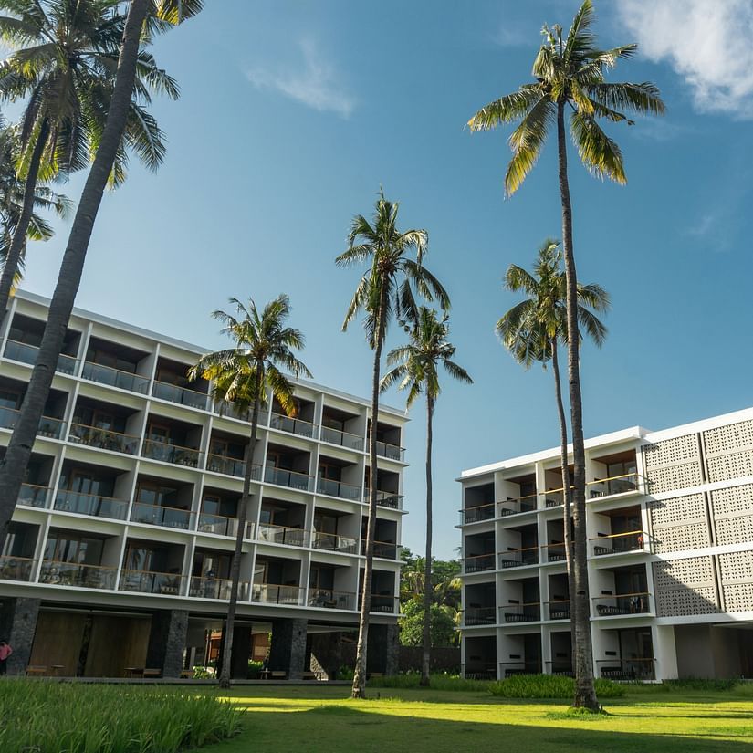 A modern building complex with palm trees under a blue sky.