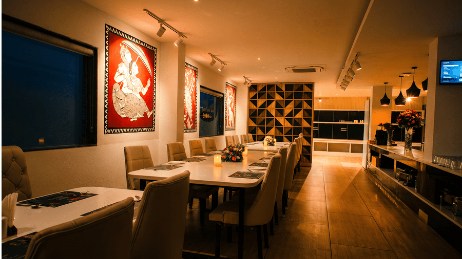 Candlelit tables with flower arrangements and red folk-art panels at Tandoori Tamashaa restaurant by night at Ilara Hotels & Spa, Tada.