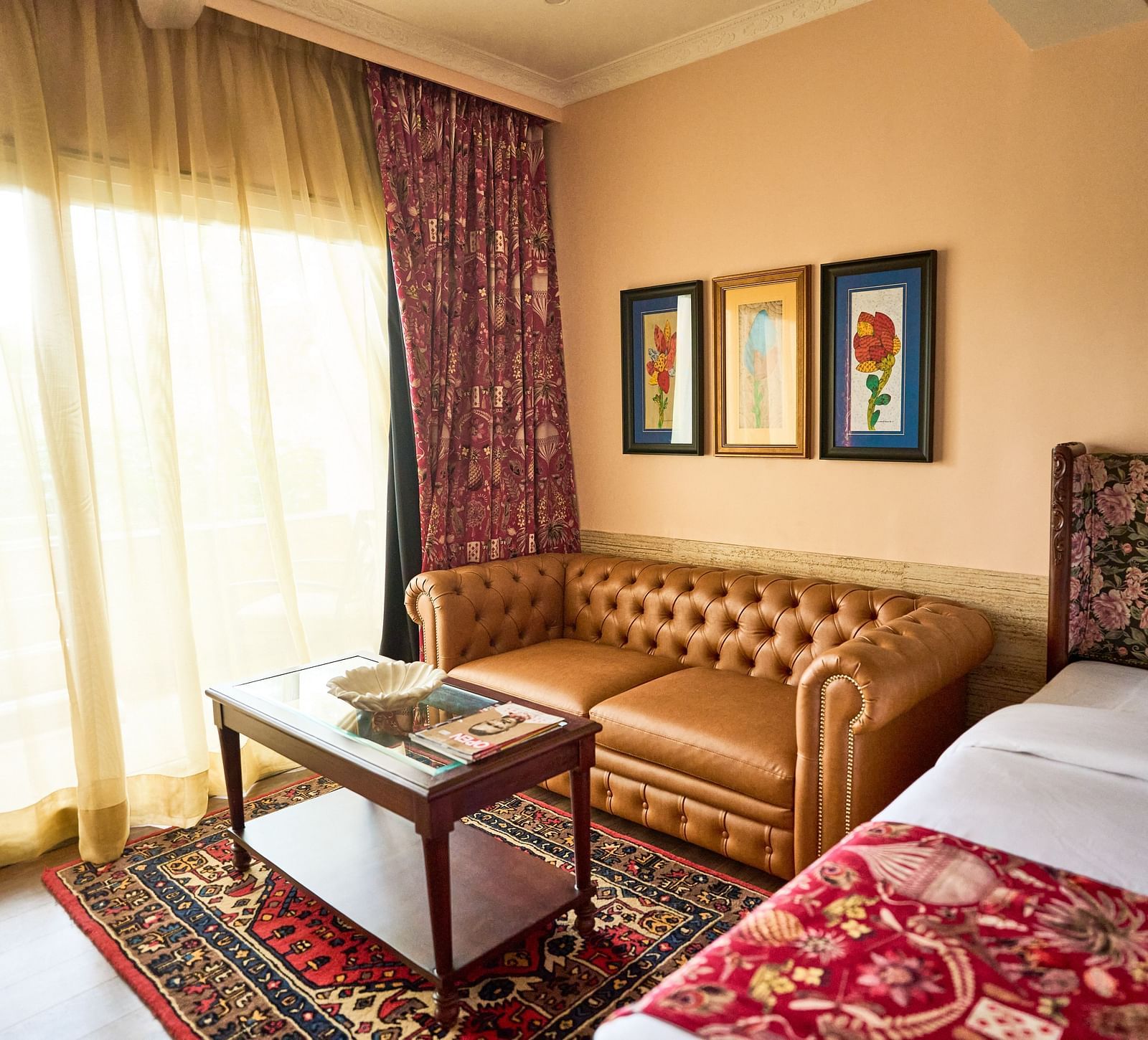 A spacious room featuring a bed on one side, a cushioned sofa on the other, and a glass table near the window adorned with closed curtains at Mayfair Manor, Alibag