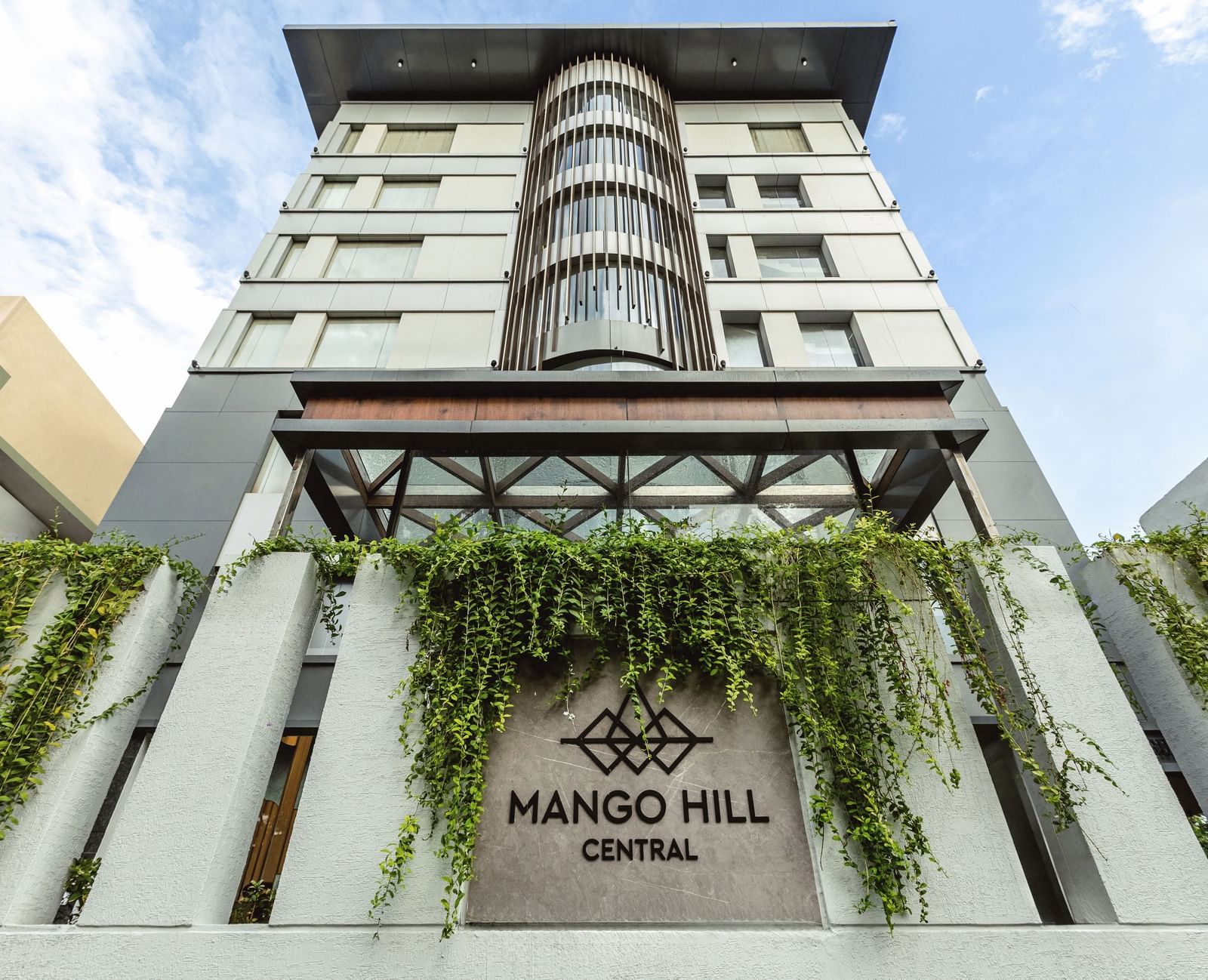 A straight-on exterior view of Mango Hill Central, Chennai, showing the multi-story building facade and the hotel name on the wall.
