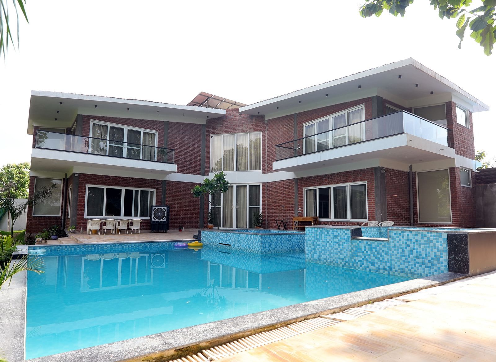 Outdoor swimming pool in front of a two-storey villa surrounded by greenery at Tisya Farms, Gurgaon.