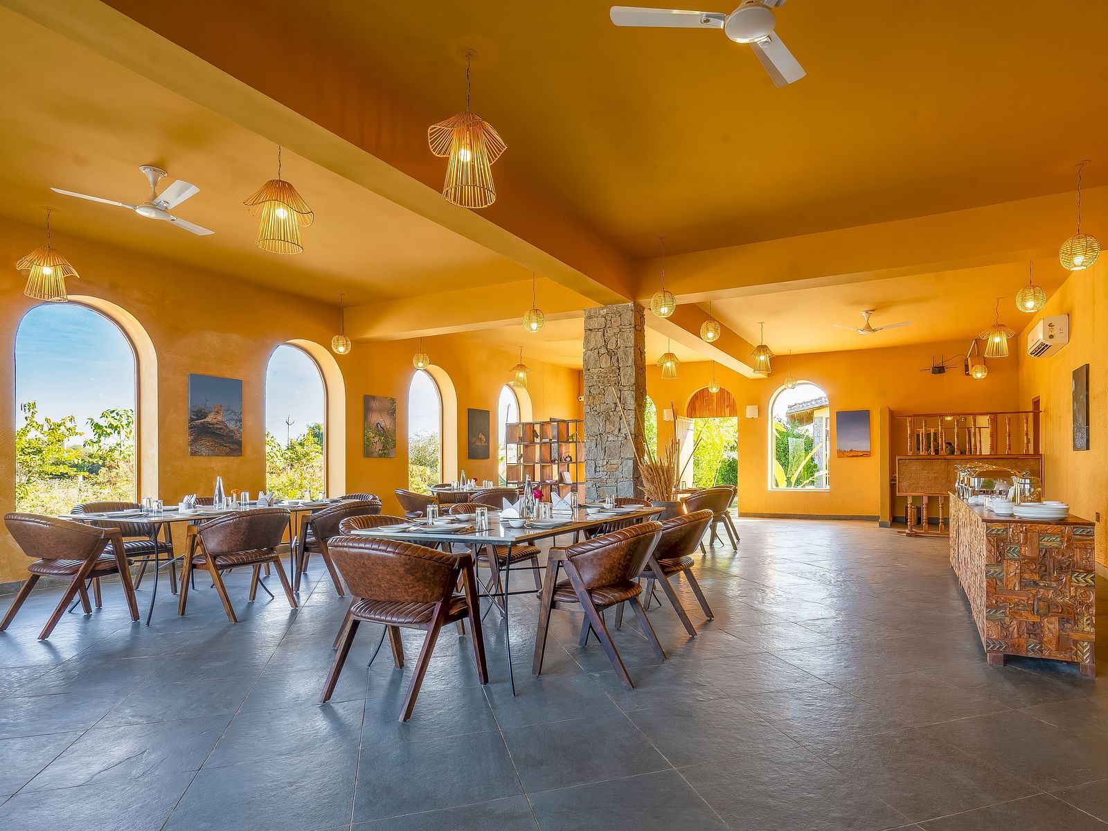 An image of L cave restaurant with boho set up featuring several sets of tables and chair,  lamp lights hanging from the ceiling, photo hanged on the walls and several open entrances - Kurja Jawai