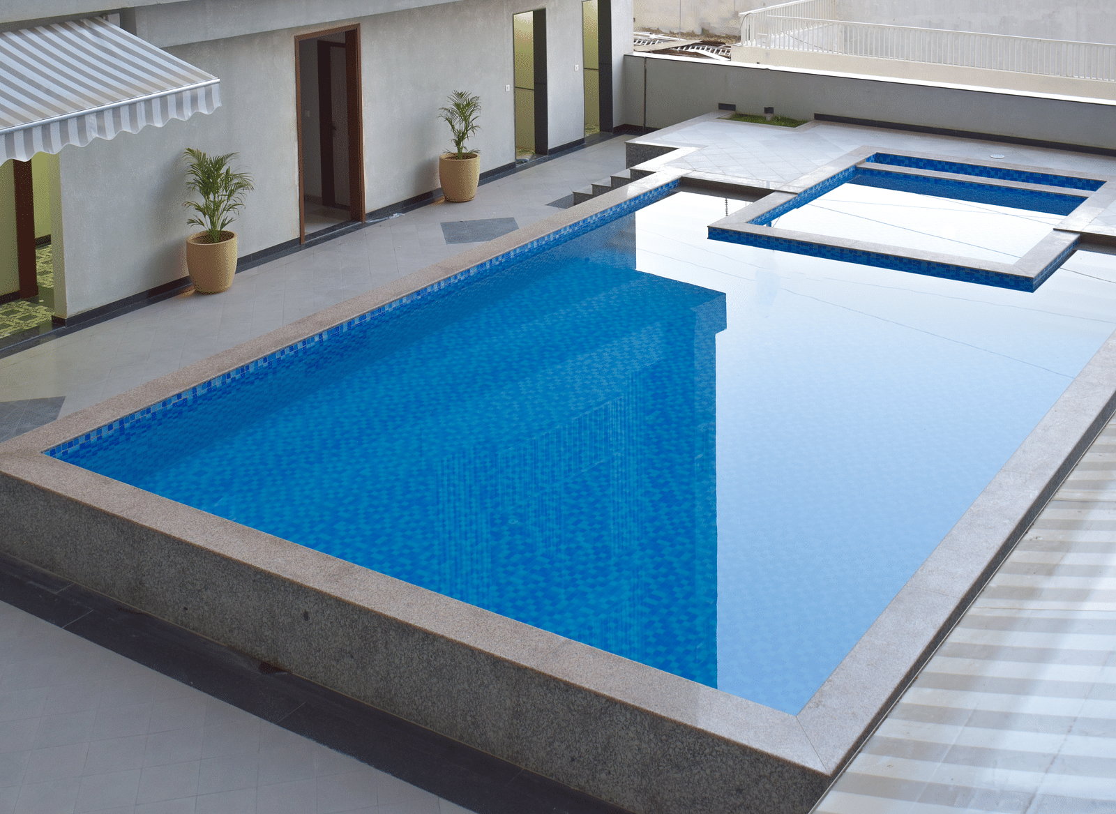 An outdoor swimming pool with blue tiles, surrounded by a concrete patio and potted plants - Urban Suites by BluSalzz, Jaipur
