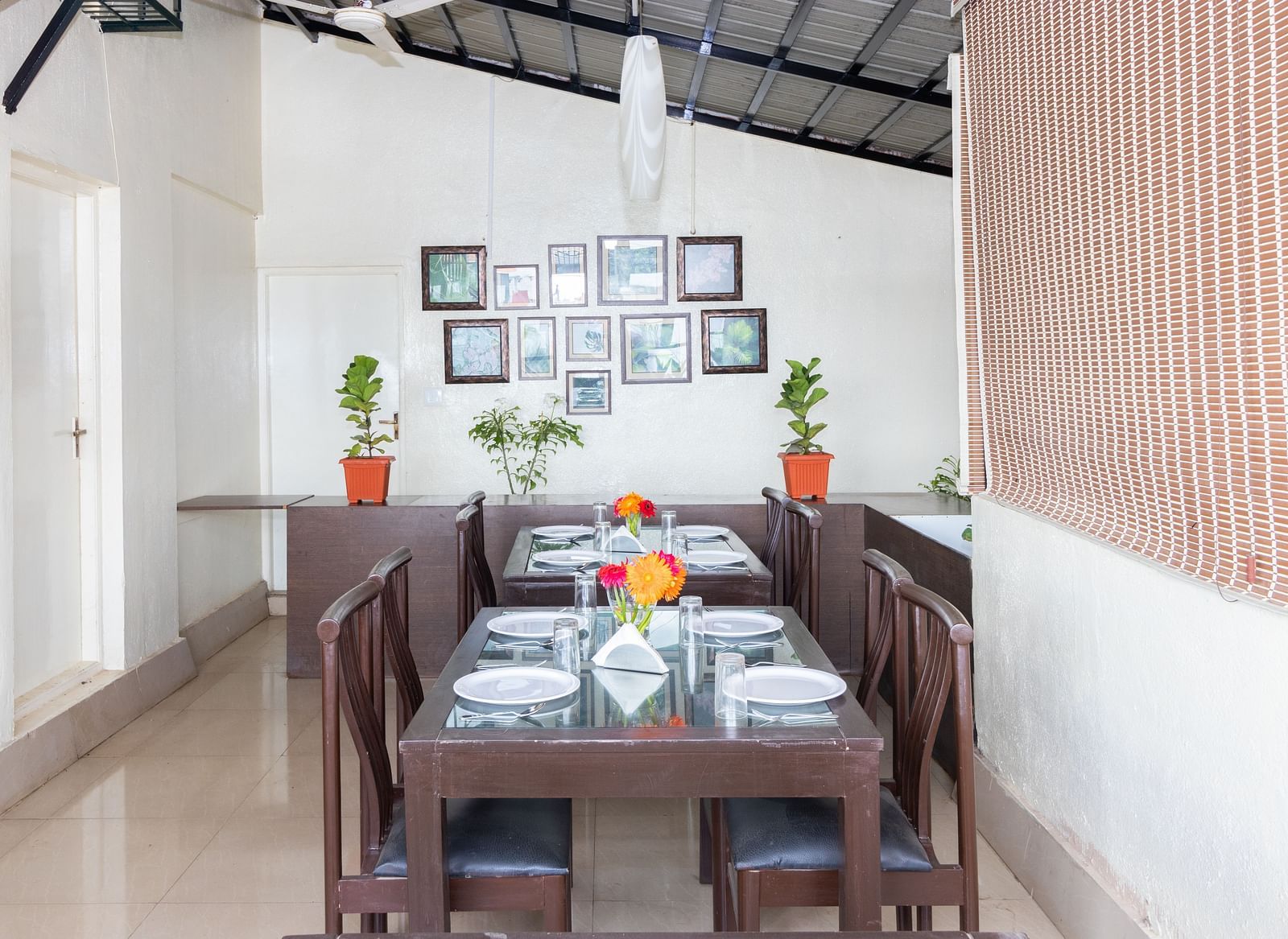 A dining area with a wooden table, chairs, and decorated with framed pictures and potted plants at Sanctum Suites Domlur, Bangalore.