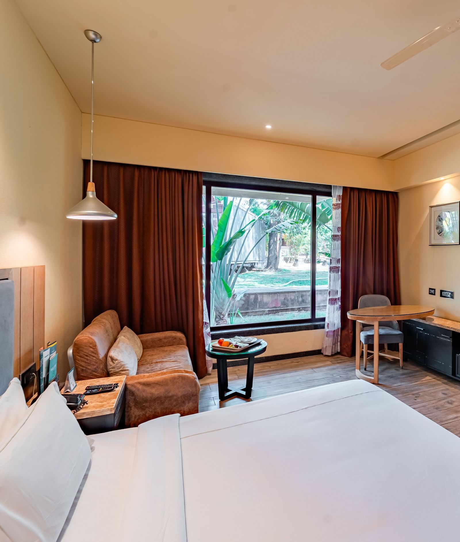 Club Room features a spacious bed, cushioned sofa, wall-mounted television, and a large window showcasing a natural view at Crescent Spa & Resort, Indore