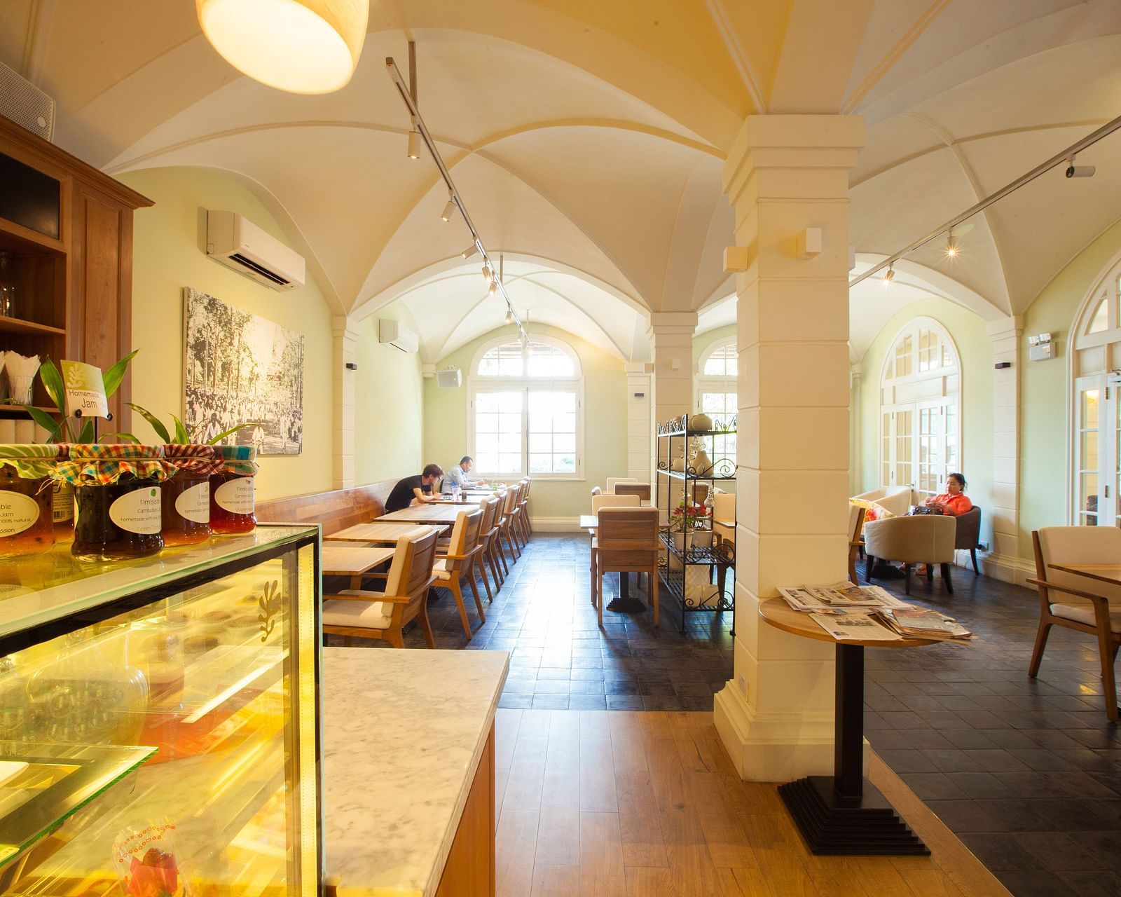A cafe interior with tables and chairs, display shelves, and a long counter | The Shop | Central Mansions, Phnom Penh