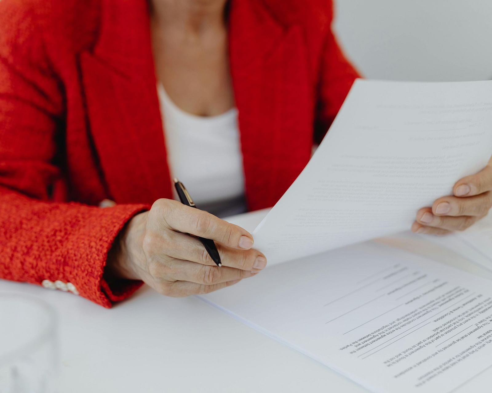 A person in a red blazer reviewing documents or papers on a desk.