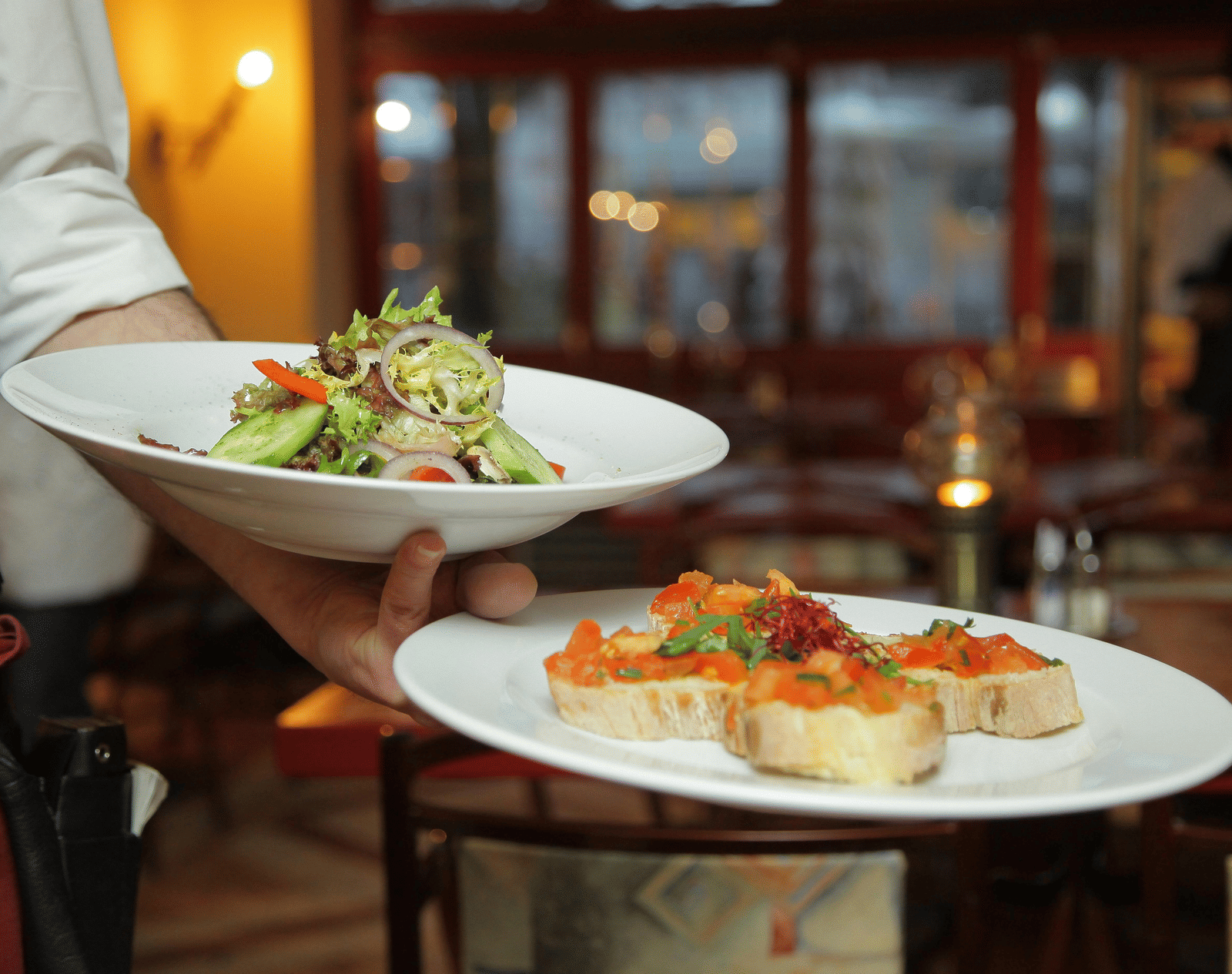 a person in a restaurant holding two plates with delicious cuisines in it that are well plated