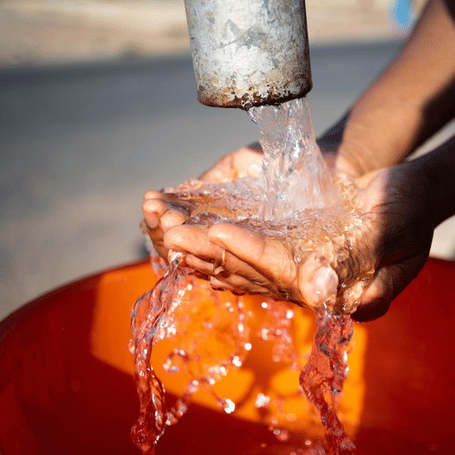 A person washes their hands under a tap, with water flowing into an orange basin.