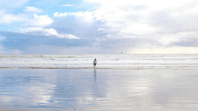 A person walking towards the ocean at a beach on a cloudy day