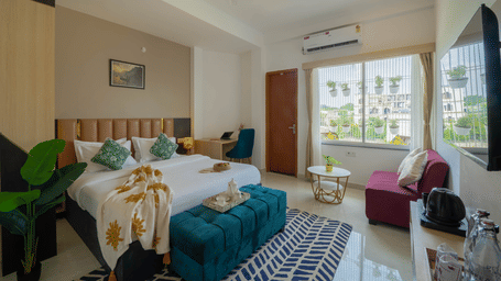 A bedroom featuring a king size bed, sofa, wall-mounted TV, indoor plants, and window view at Perfectstayz Premium Kaashin, Varanasi.