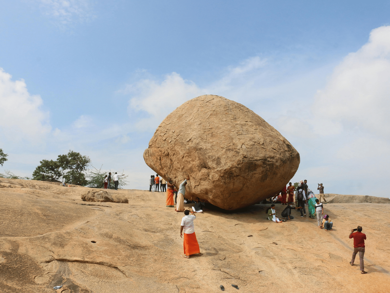 A large boulder sits on a hill, with people around the base.