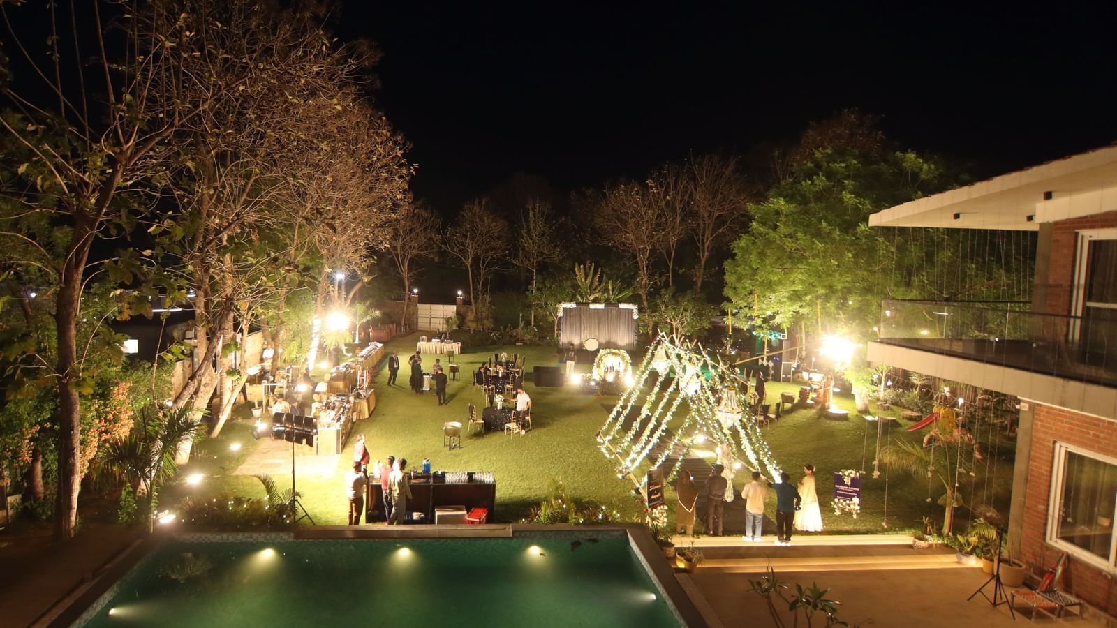 Elevated poolside view at night with event lighting and lawn setup at Tisya Farms, Gurgaon.