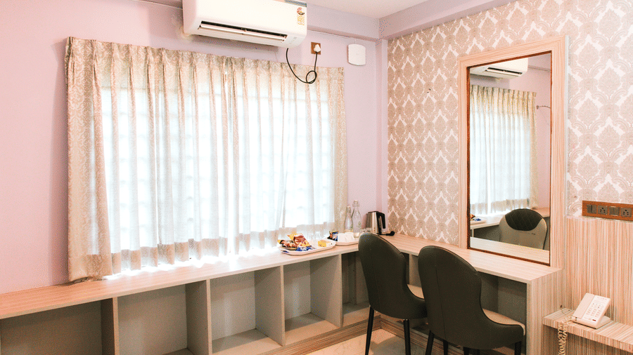 A section of a room with a window, curtains, a wall-mounted air-conditioner, and a dressing table with two chairs | Vintage Trails By Ilara