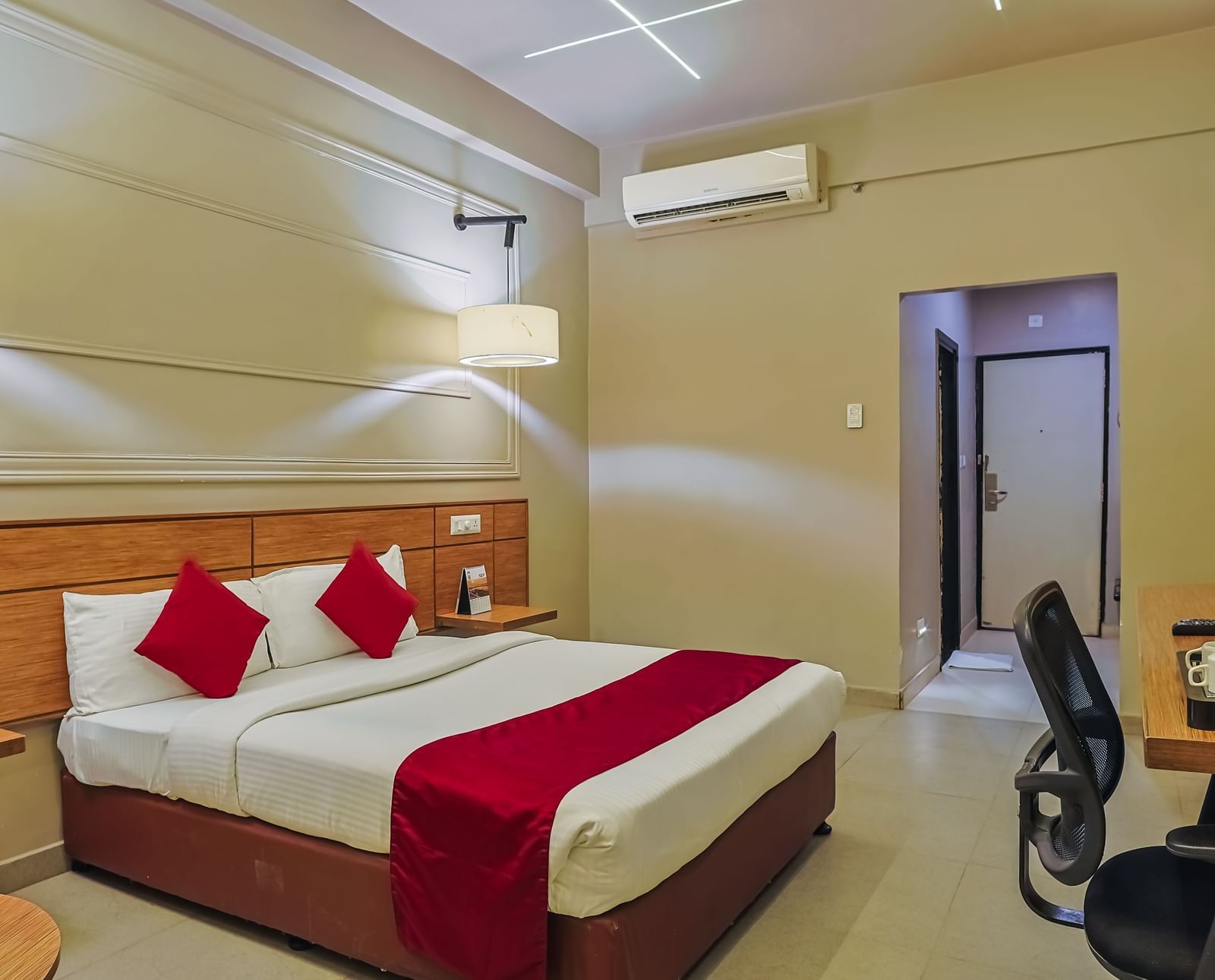 Bedroom with double bed, red runner, pillows, work desk and chair at Max Hotel Prayagraj.