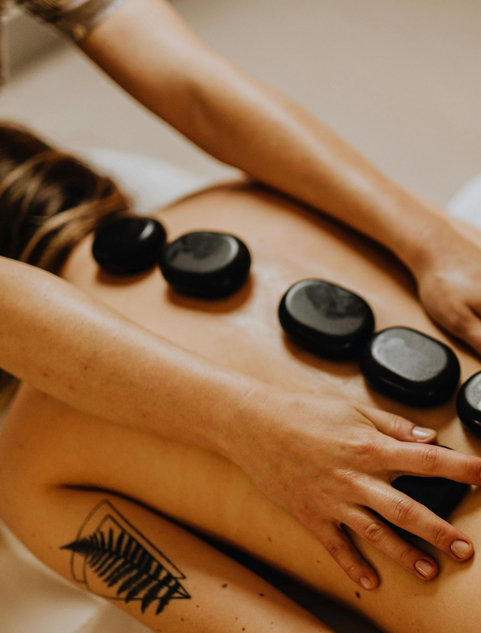 image of a woman involved in a pebble therapy with medium sized black coloured stones kept over her spine