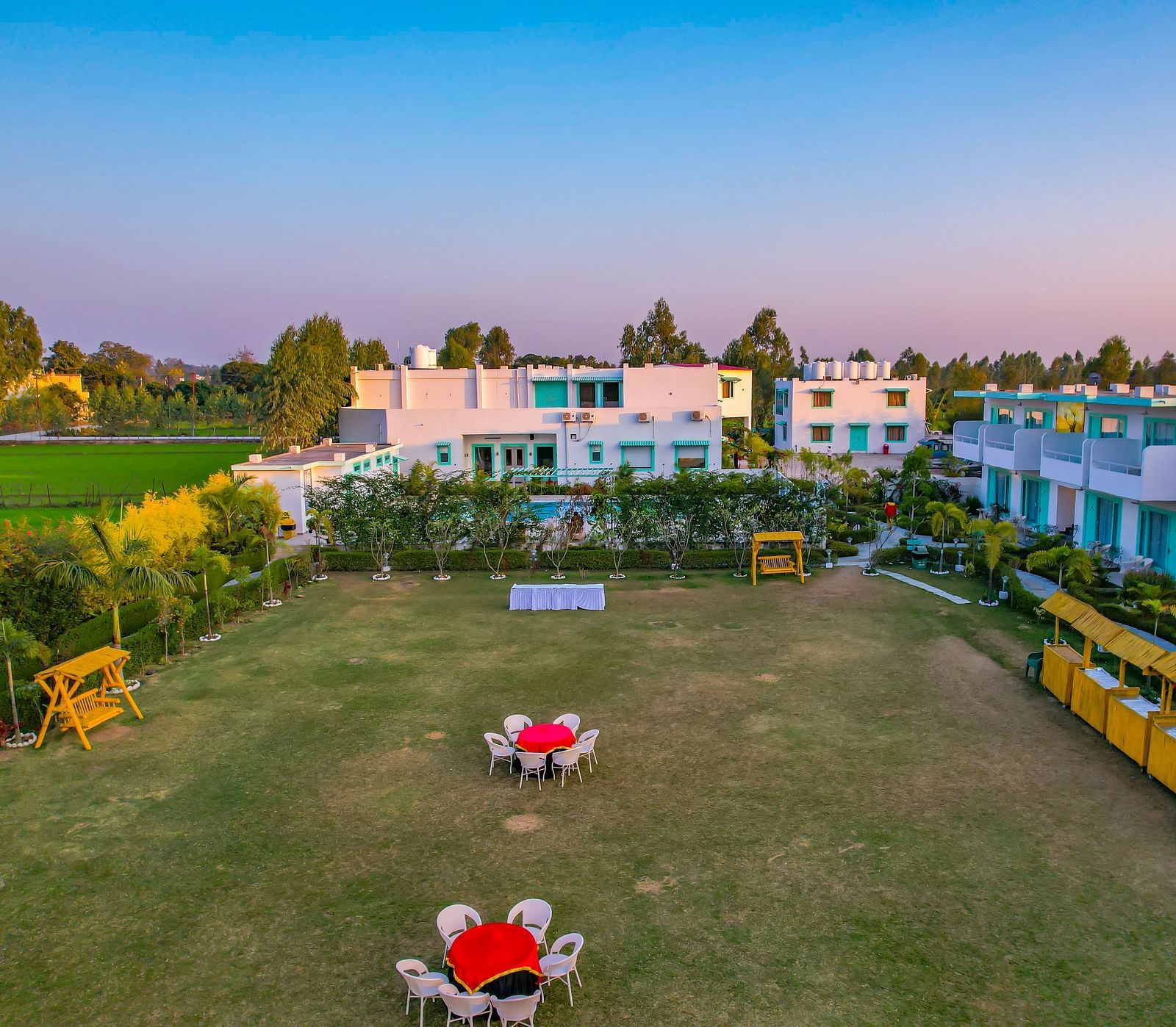 Lawn area at Vedikant Resorts The Mallard Corbett with tables and chairs set up outdoors, bordered by hedges and facing the rooms.