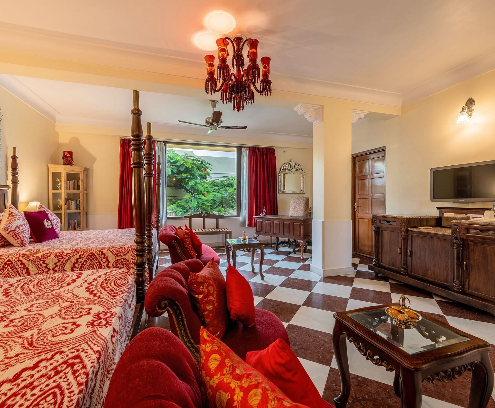 A luxurious suite at Dera Rawatsar offers two elegant beds, a comfortable seating area, a television, and striking checkered flooring.
