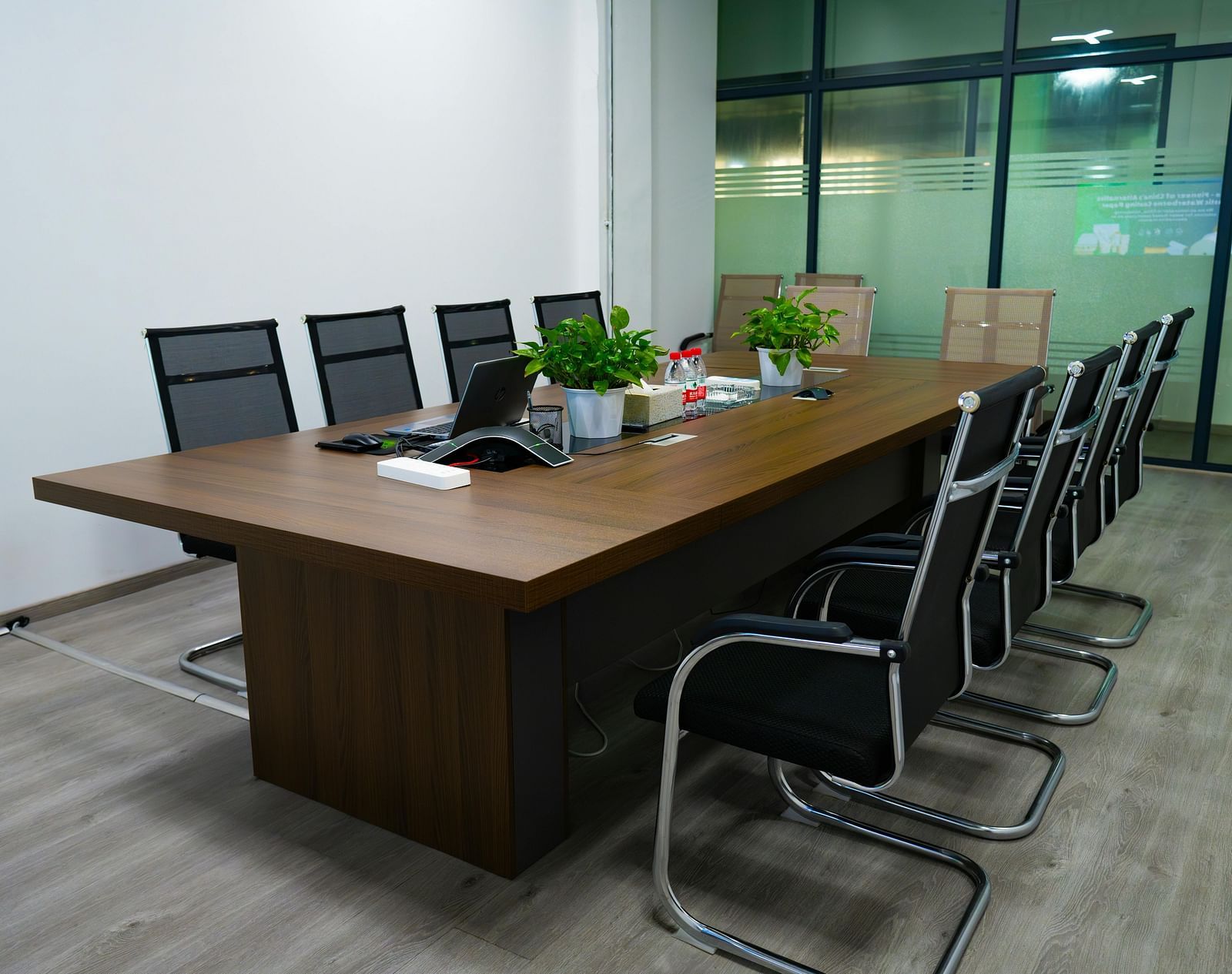 A modern meeting room with a large wooden table and several black chairs.