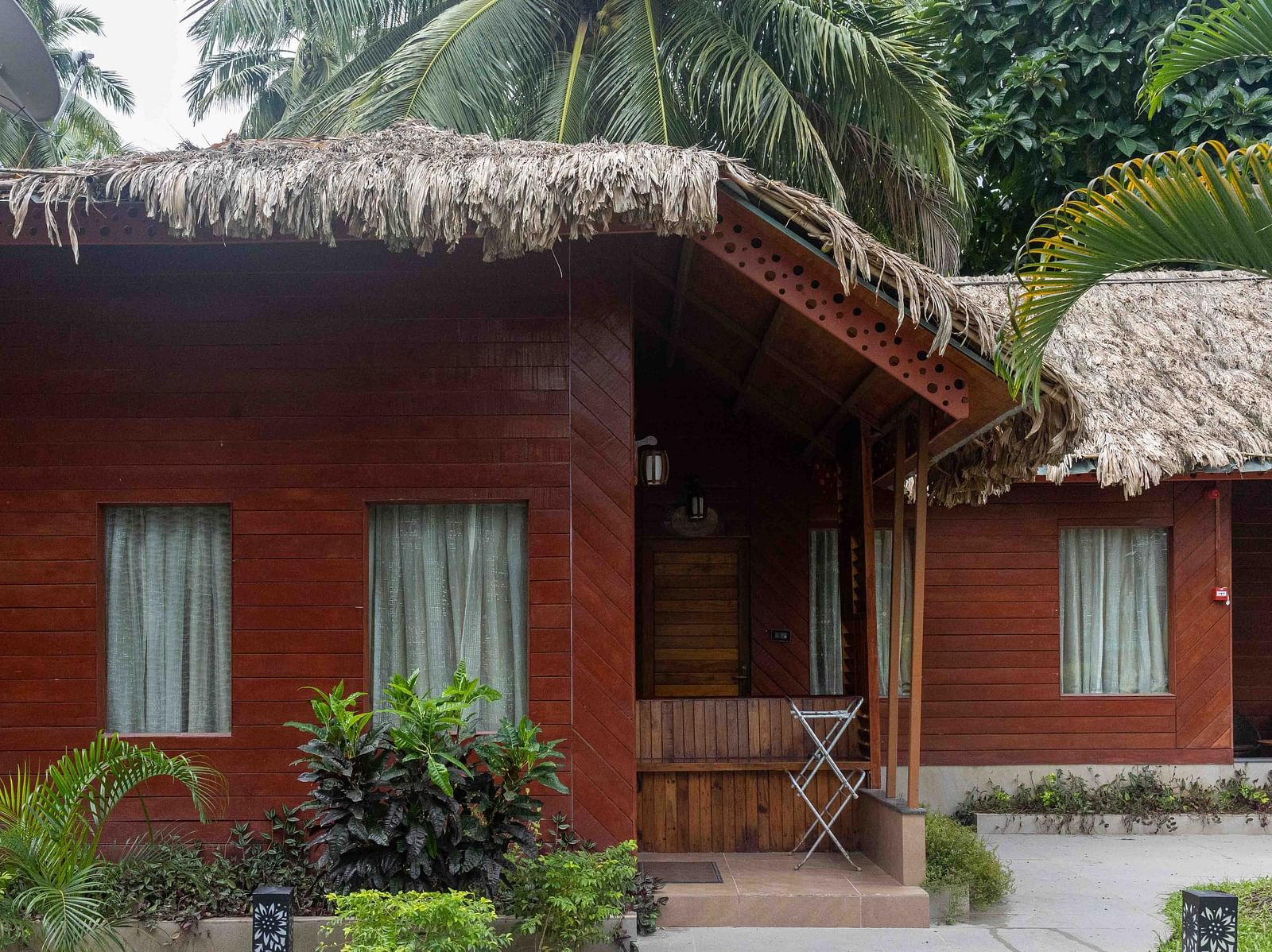 A beachside view with palm trees framing the scene. The sandy shore and calm water add to the tranquil atmosphere, with an outdoor structure in the background - Coral Reef Resort & Spa, Havelock