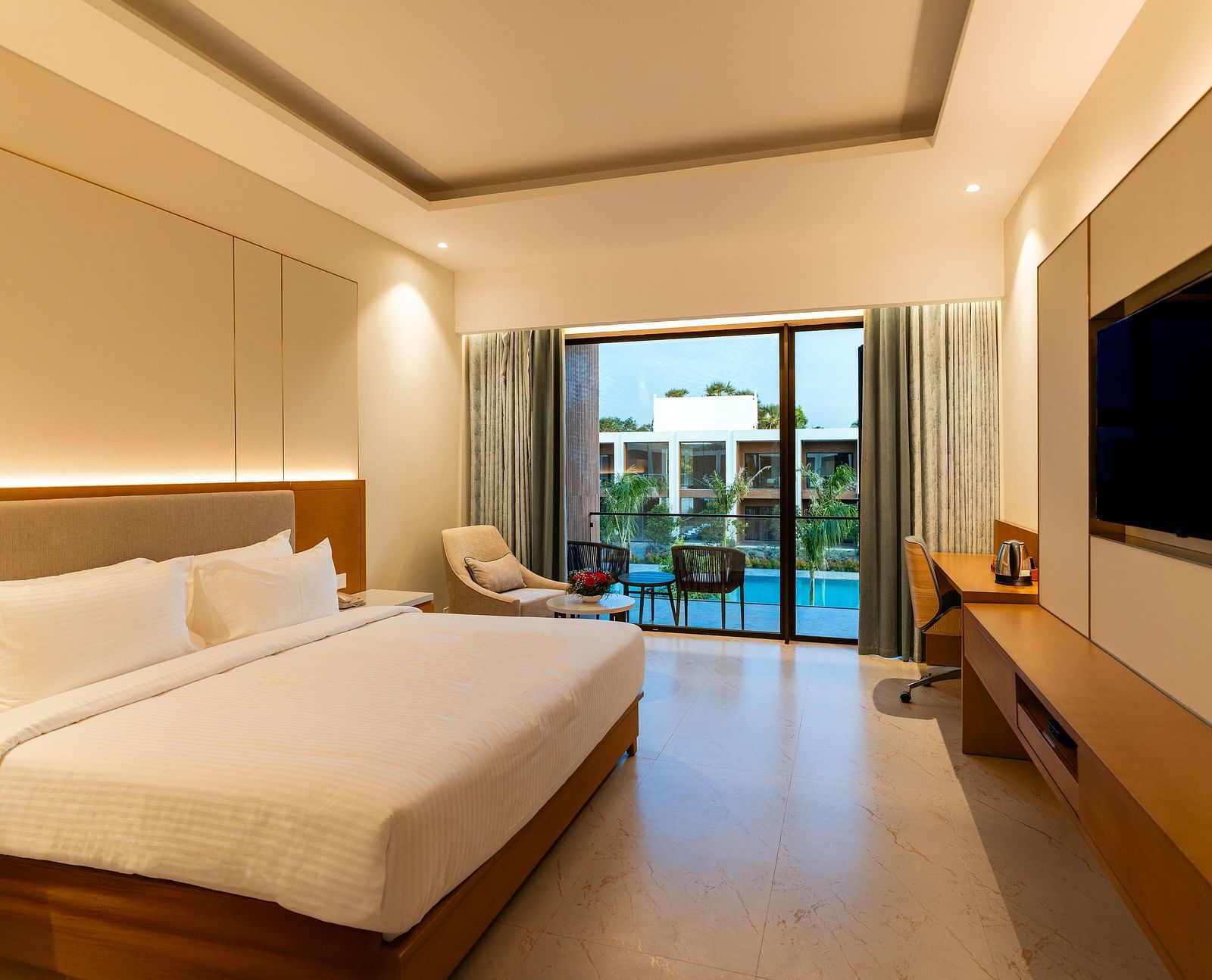 A hotel room at The Shore Trishvam, Pondicherry featuring a double size bed, flat TV screen, and a balcony arranged with two chairs. 