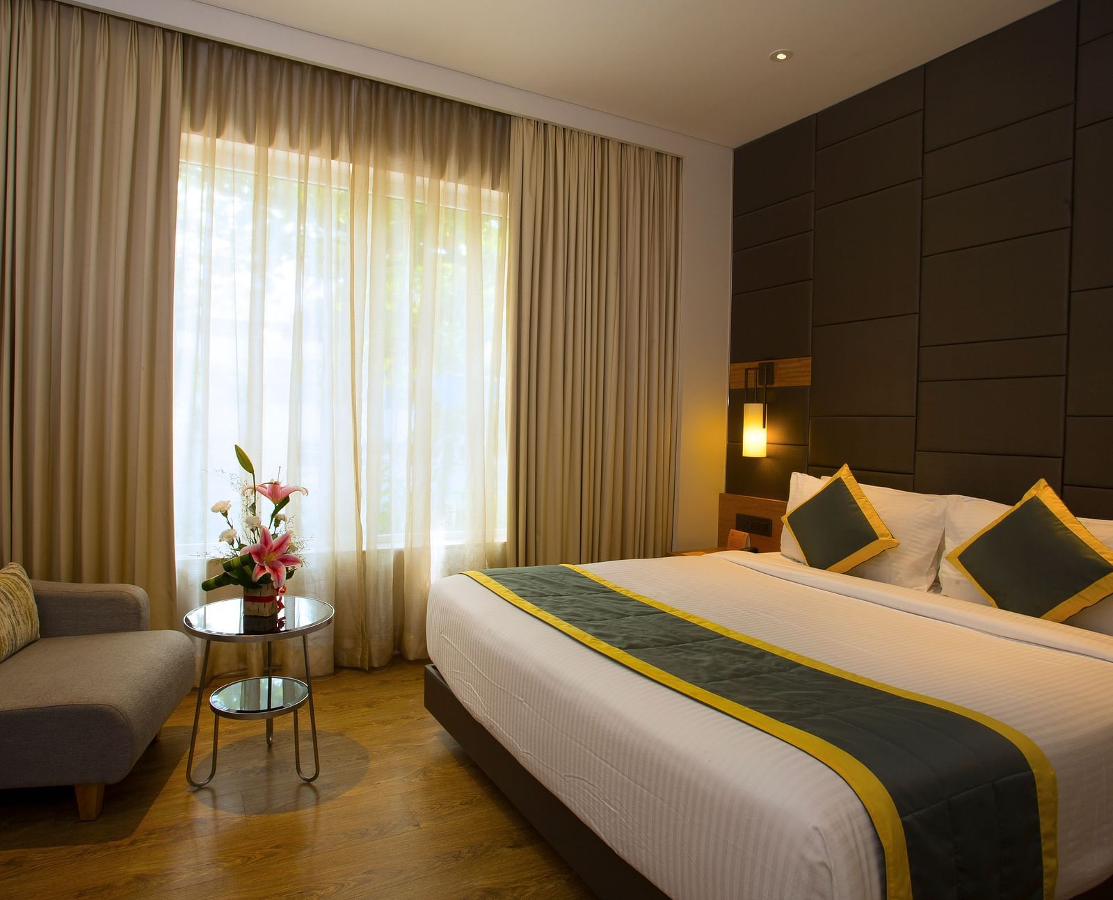 a bedroom with a large bed and a sofa opposite the the bed, with a small table in the middle - Hotel Fountain Tree By TGI - JP Nagar, Bangalore