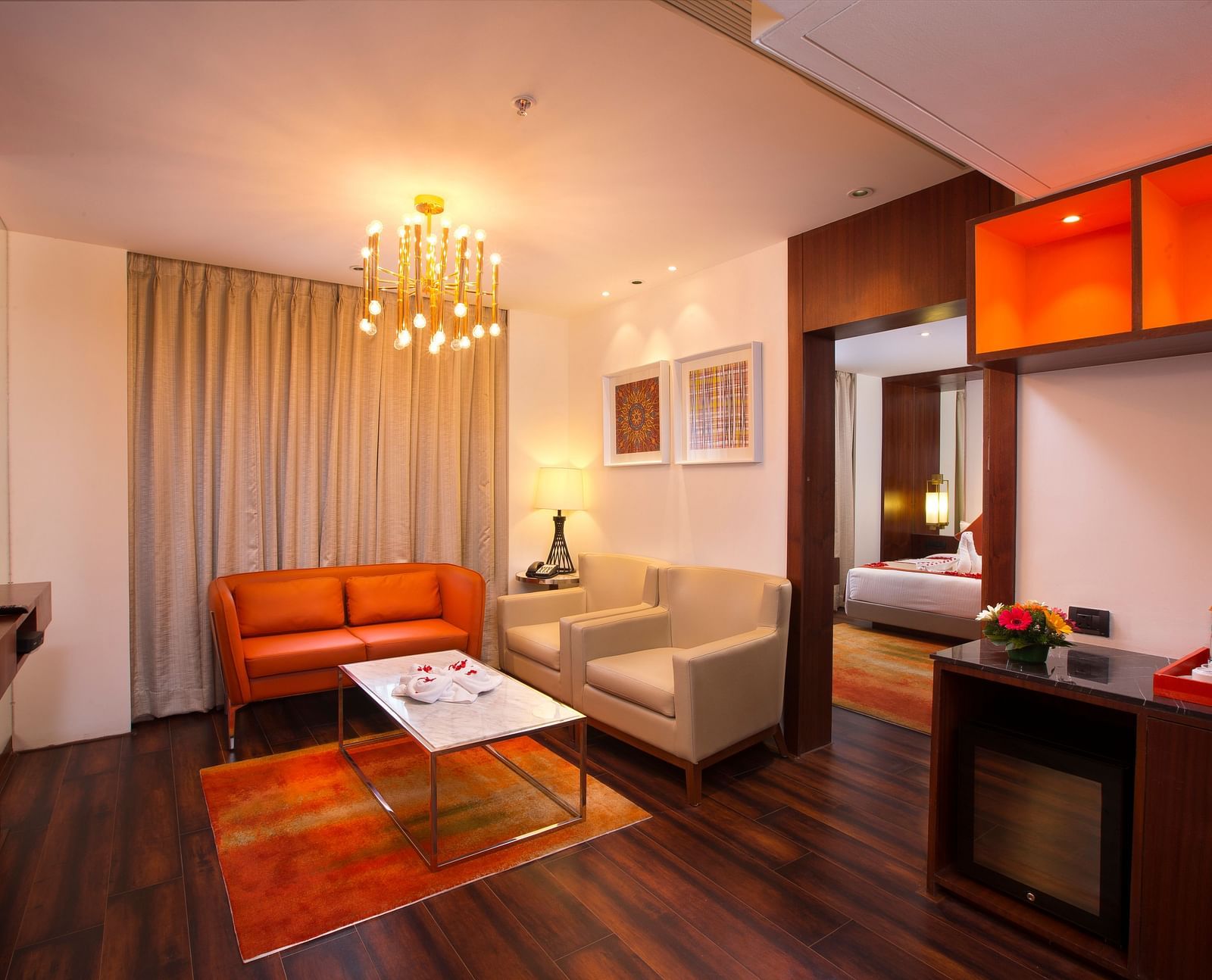 A hotel suite living area with a modern chandelier, orange leather sofa and a marble coffee table - Hotel Southend by TGI - Bommasandra, Bangalore