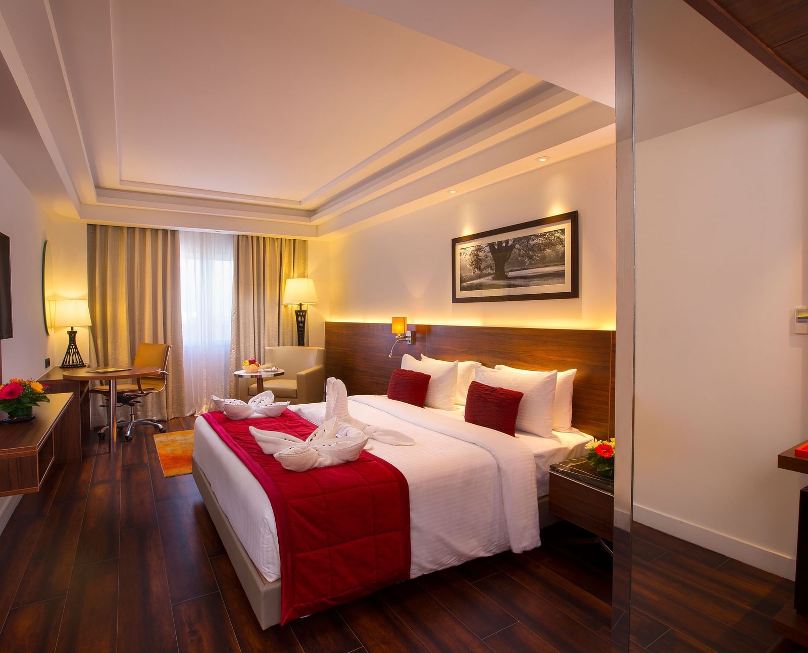 Another view of an elegant hotel room with a large bed, red throw blanket, decorative pillows and a framed black-and-white photograph on the wall - Hotel Southend by TGI - Bommasandra, Bangalore