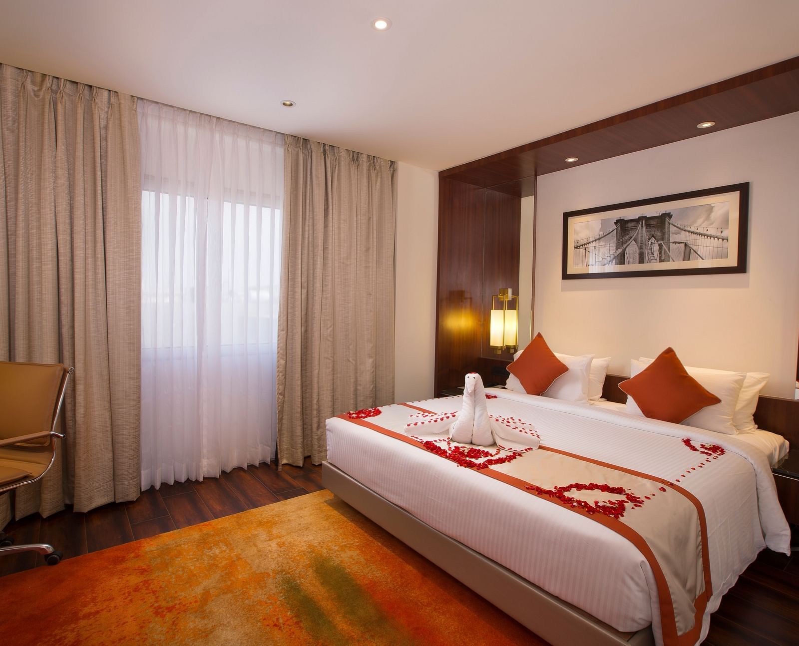 A hotel room with a large bed with white and orange linens, a brown office chair and sheer curtains over a window - Hotel Southend by TGI - Bommasandra, Bangalore