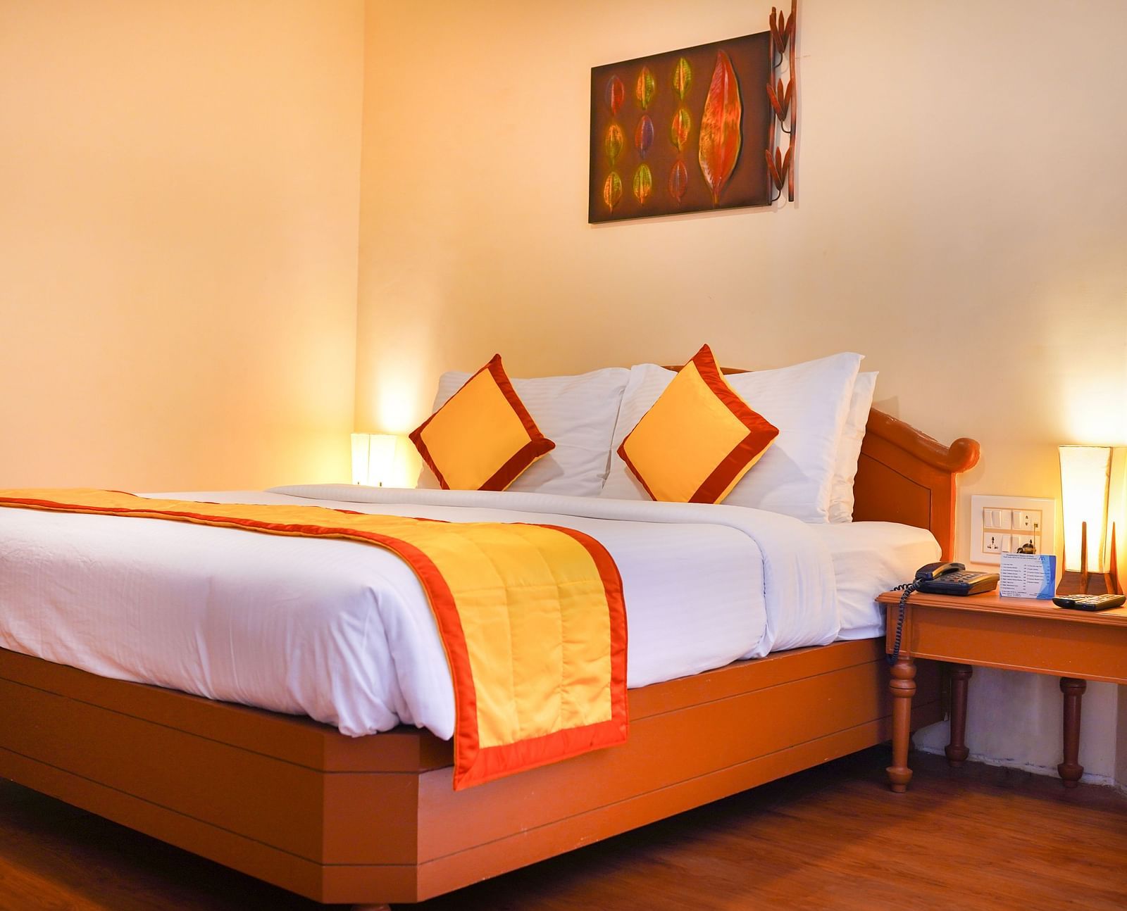 A well-appointed bedroom with a large bed, a yellow and orange bed runner, two bedside lamps, and a decorative wall hanging at La Montana By TGI, Ooty