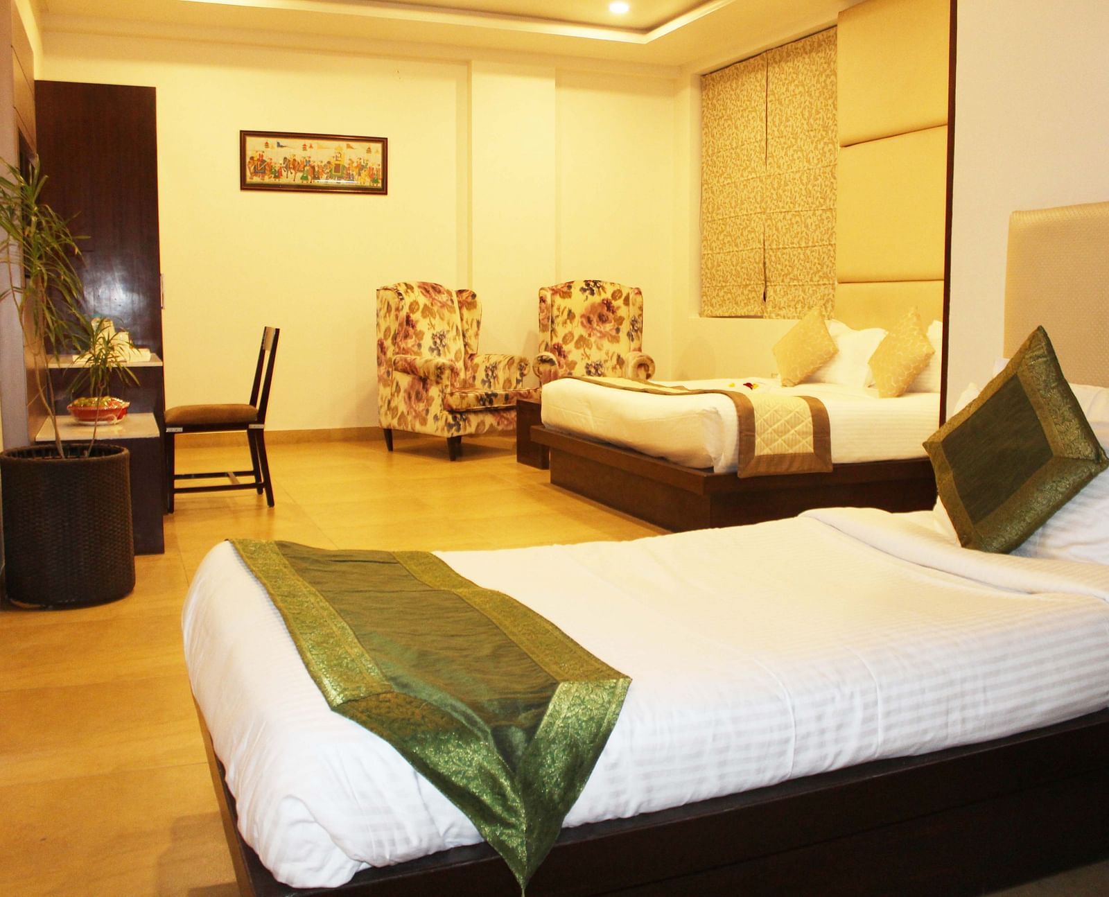 Another view of a spacious hotel room with two armchairs, a large bed with white linens and patterned wallpaper - TGI Apple Inn, Jaipur 