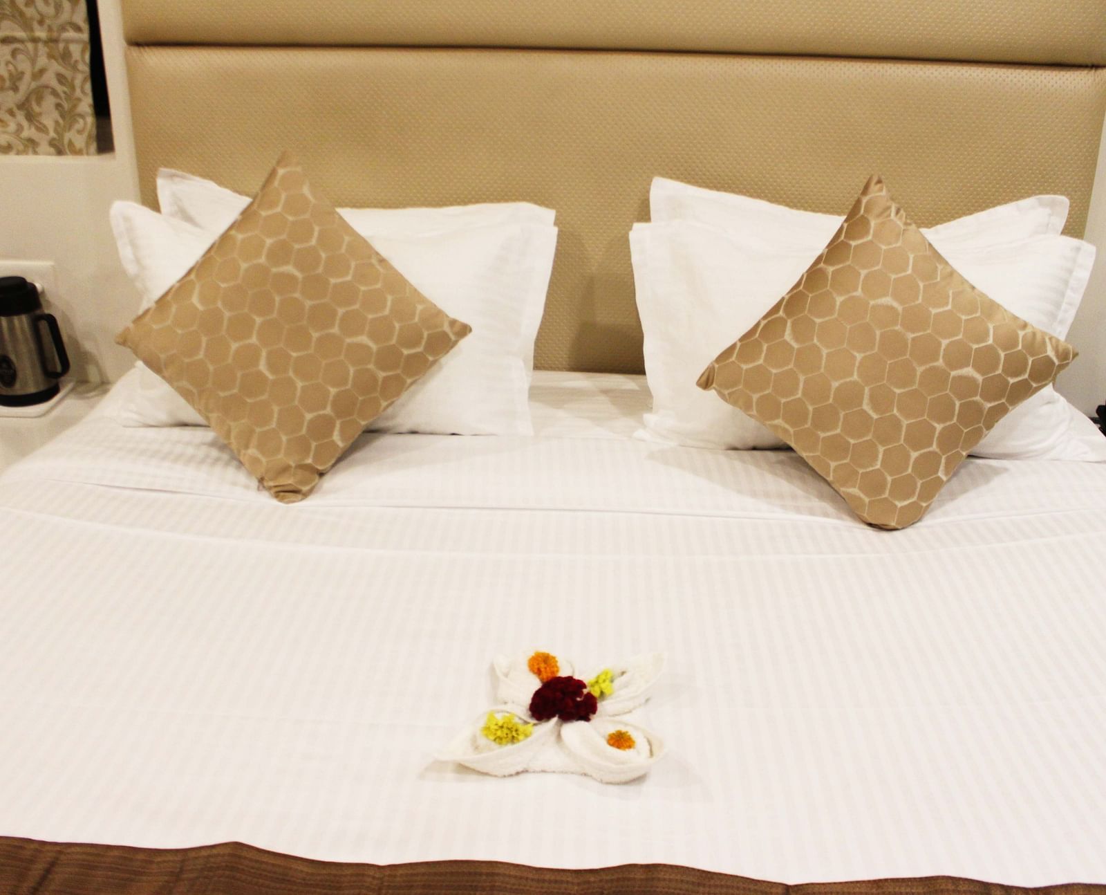 A image of the bed with plush pillows and a elegant design made out of towel and flowers placed on the breadspread - TGI Apple Inn, Jaipur 