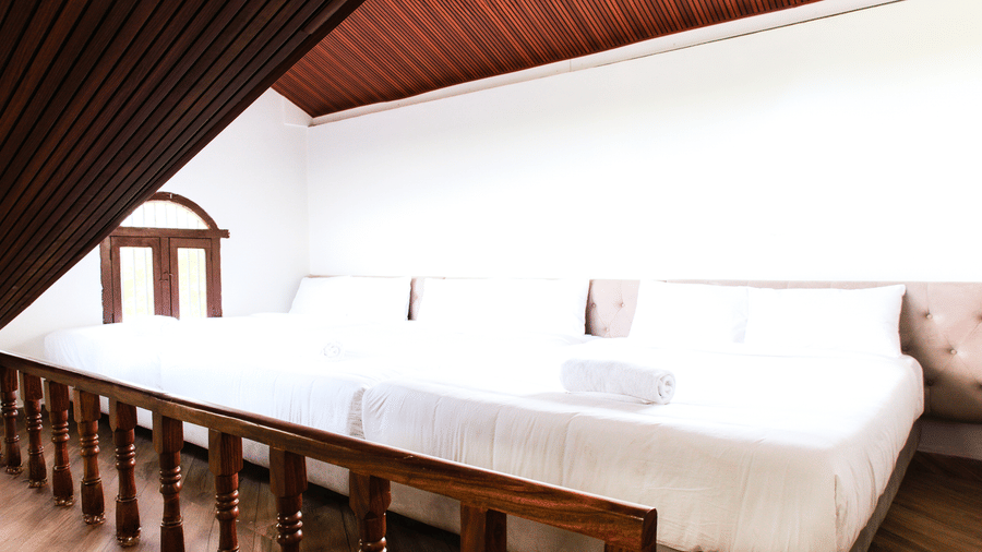 A mezzanine sleeping area featuring a bed with white linen, a wooden ceiling, and a wooden railing overlooking the lower floor | Vintage Trails By Ilara