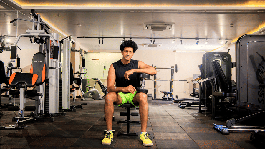 Guest seated holding a dumbbell between multi-gym strength machines and mirrored walls in the amber-lit fitness centre at Ilara Hotels & Spa, Tada.