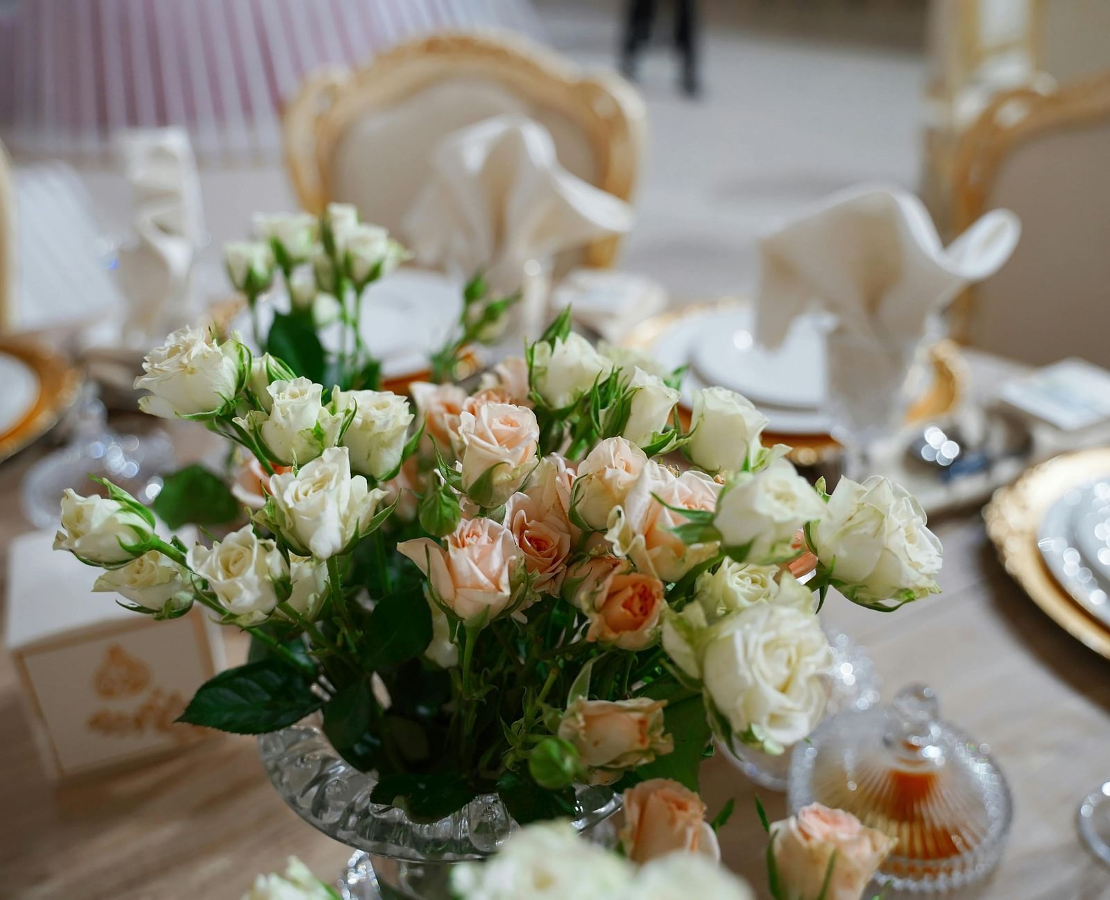 A close up shot of a beautiful flower vase with a lot of white and pink roses on a dining table.
