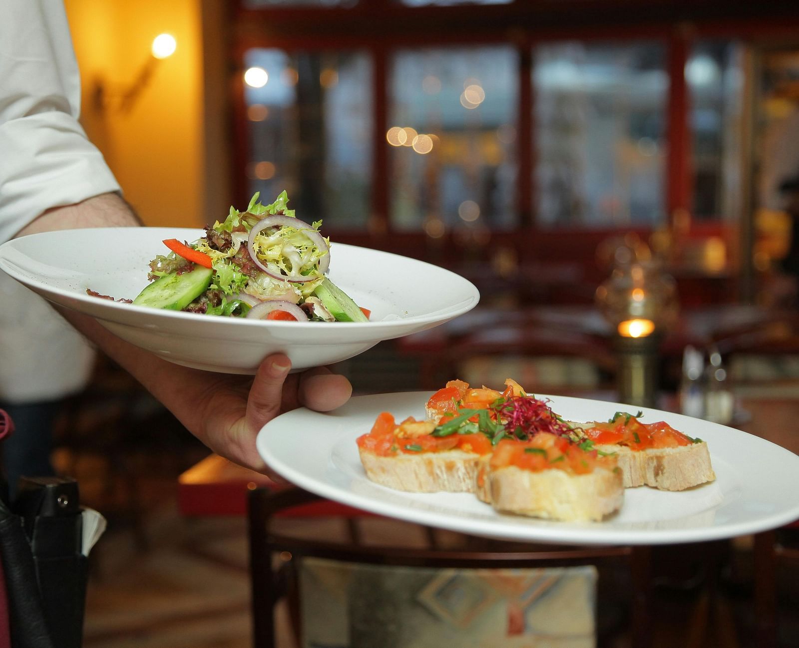 A person in a restaurant holding two plates with delicious cuisines in it that are well plated.