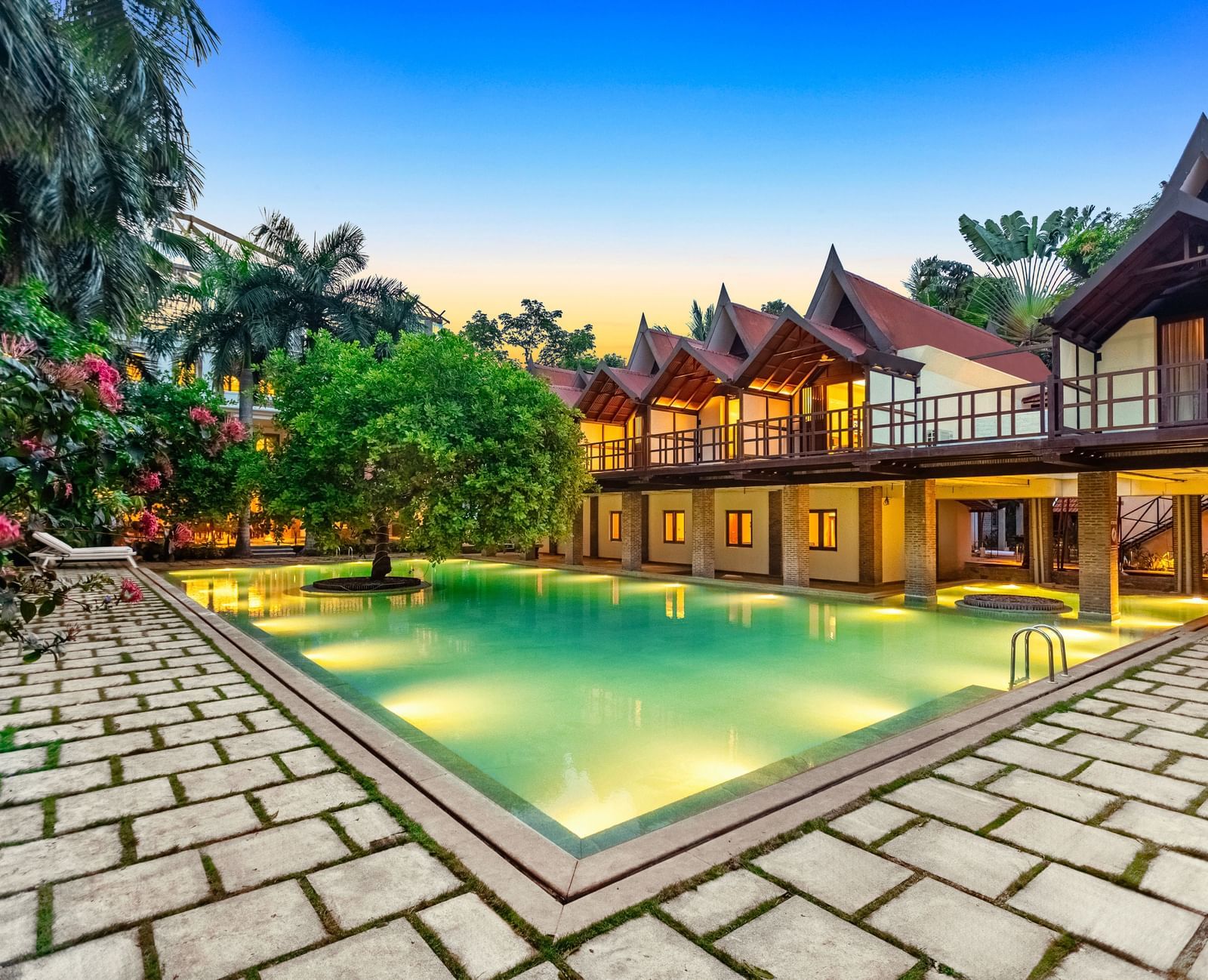 Twilight descends over the beautifully lit pool and traditional villas at Mango Hill Auroville, Pondicherry.