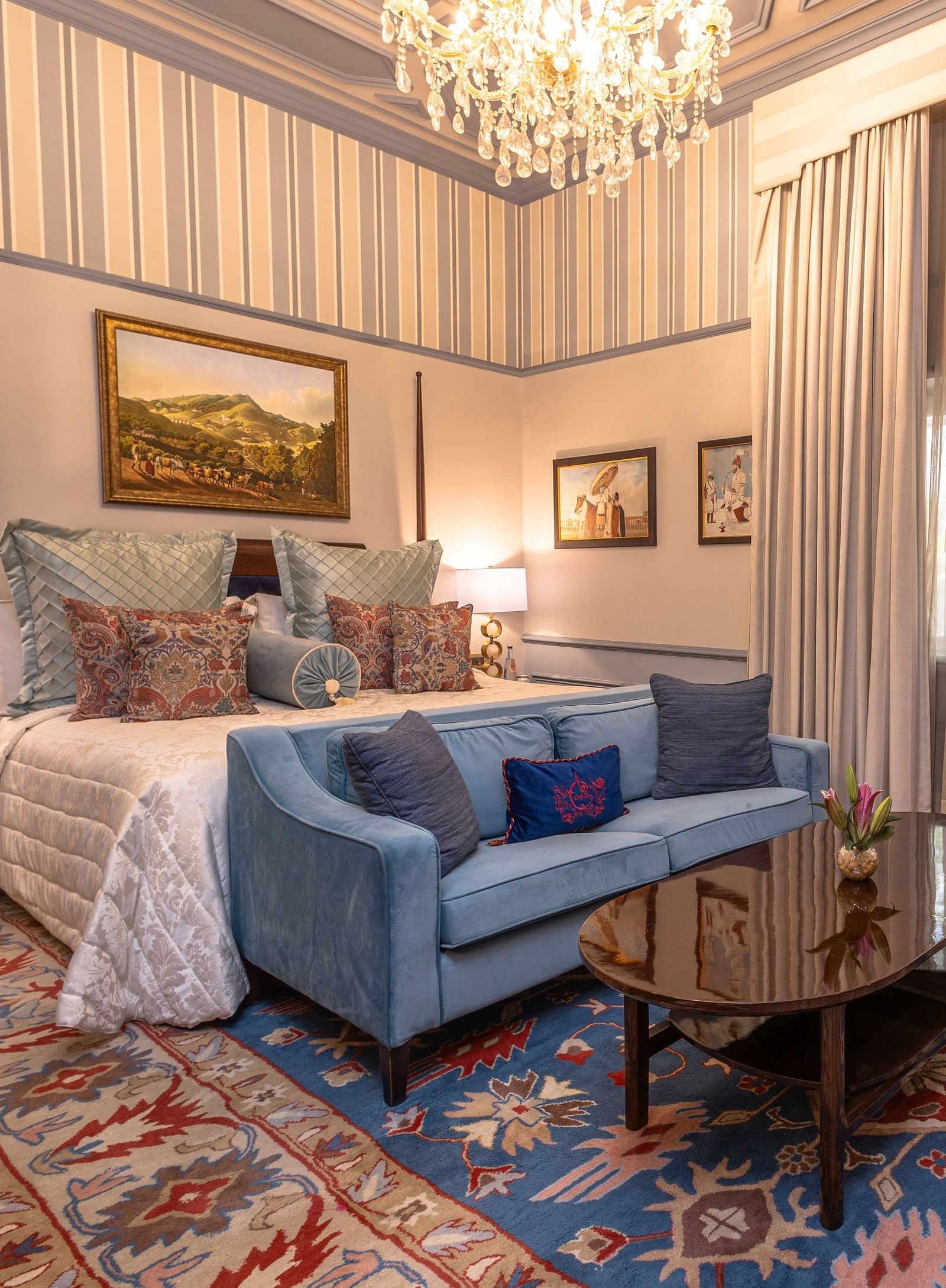 image of the brightly lit bedroom with a king size bed and blue couch place in front of the bed at our heritage parlour suites - The Claridges New Delhi