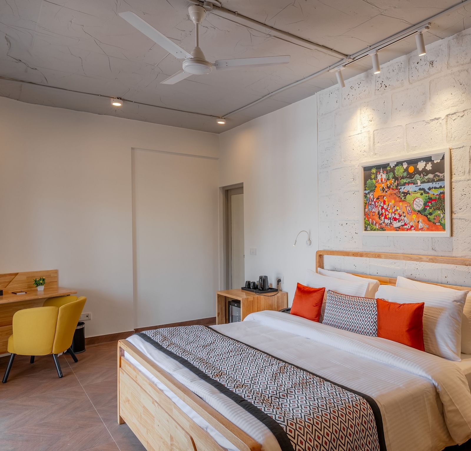 An image of hotel room with king size bed, painting on the wall, work desk and chair at one corner and a bedside table  at Bedzzz Xclusiv Morjim, Goa