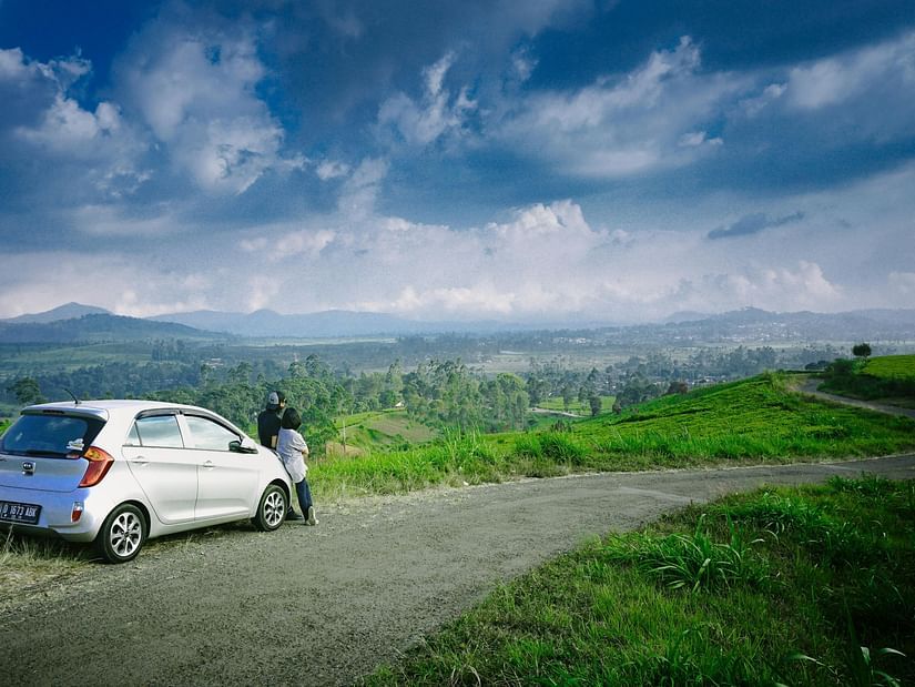 A car parked on a scenic hillside road with lush greenery and mountains.